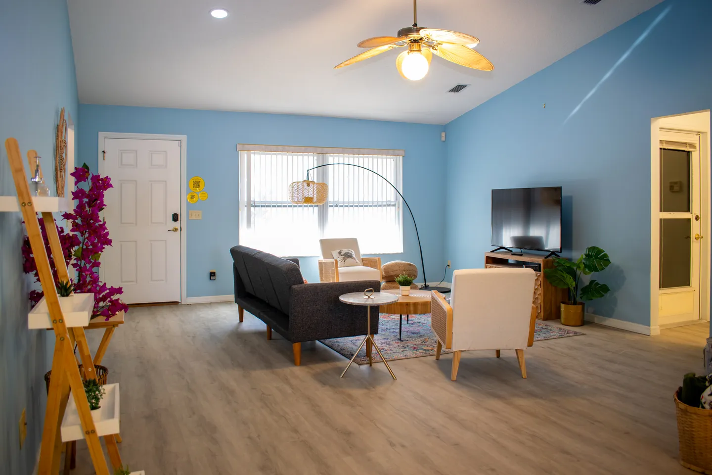 Living room with light blue walls, a dark grey sofa, armchairs, an arched floor lamp, and a mounted flat-screen TV.