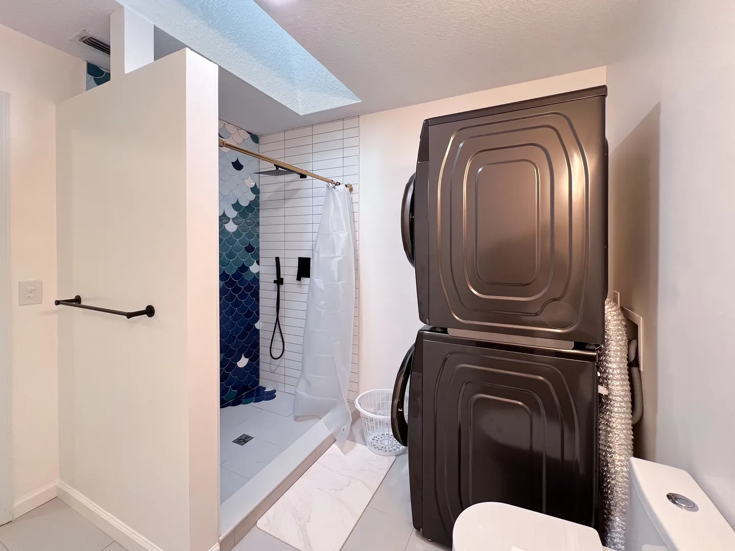 Bathroom with a walk-in shower featuring blue fish-scale accent tiles, white wall tiles, and a stacked washer and dryer unit.
