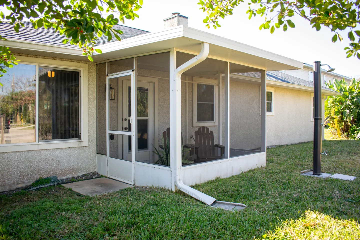 Exterior view of a home with a screened-in porch and an outdoor shower in the grassy yard.