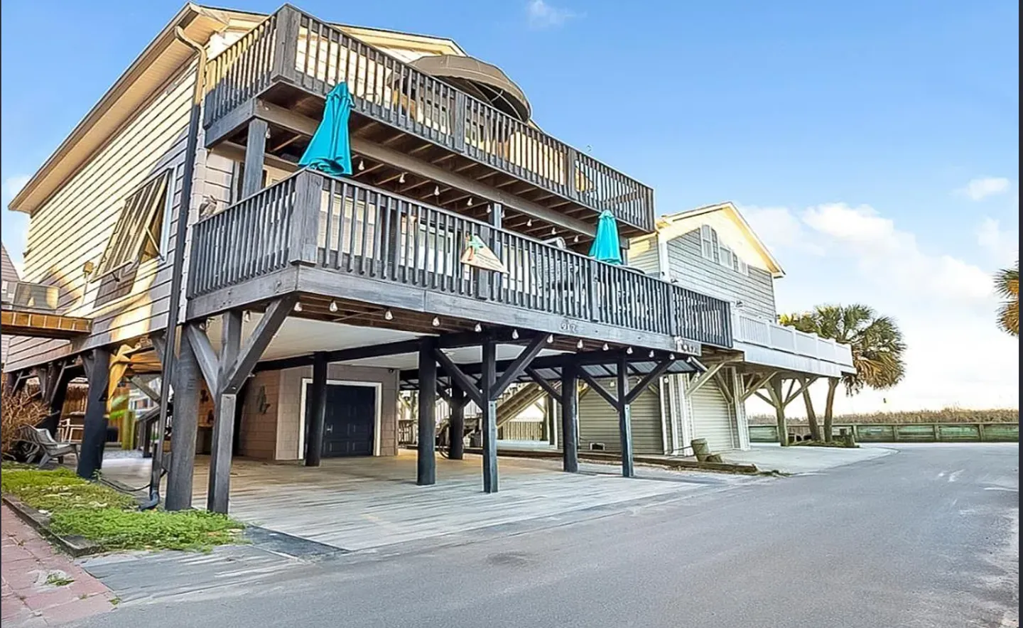 Exterior view of a multi-story stilt home with covered parking below and two levels of wooden balconies.