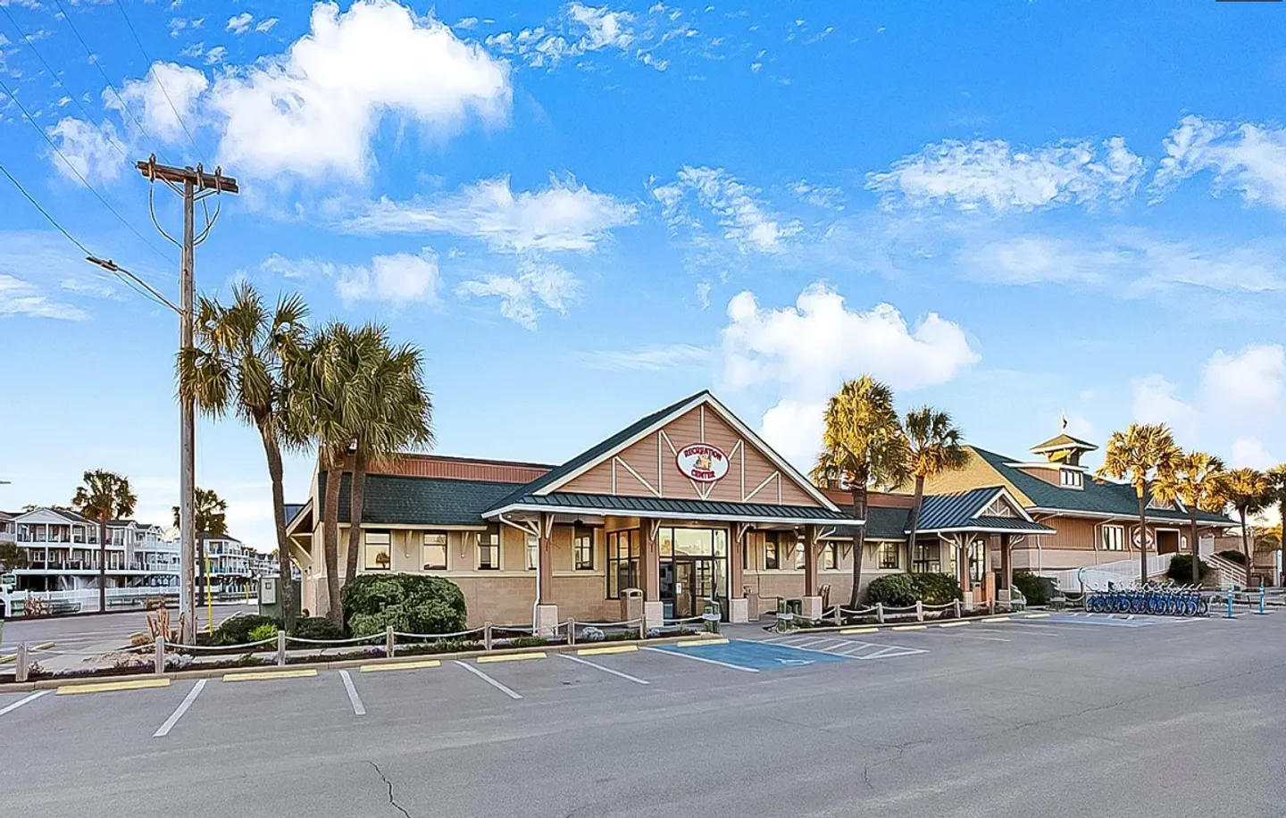 Exterior view of a community recreation center building and parking lot under a blue sky with palm trees.
