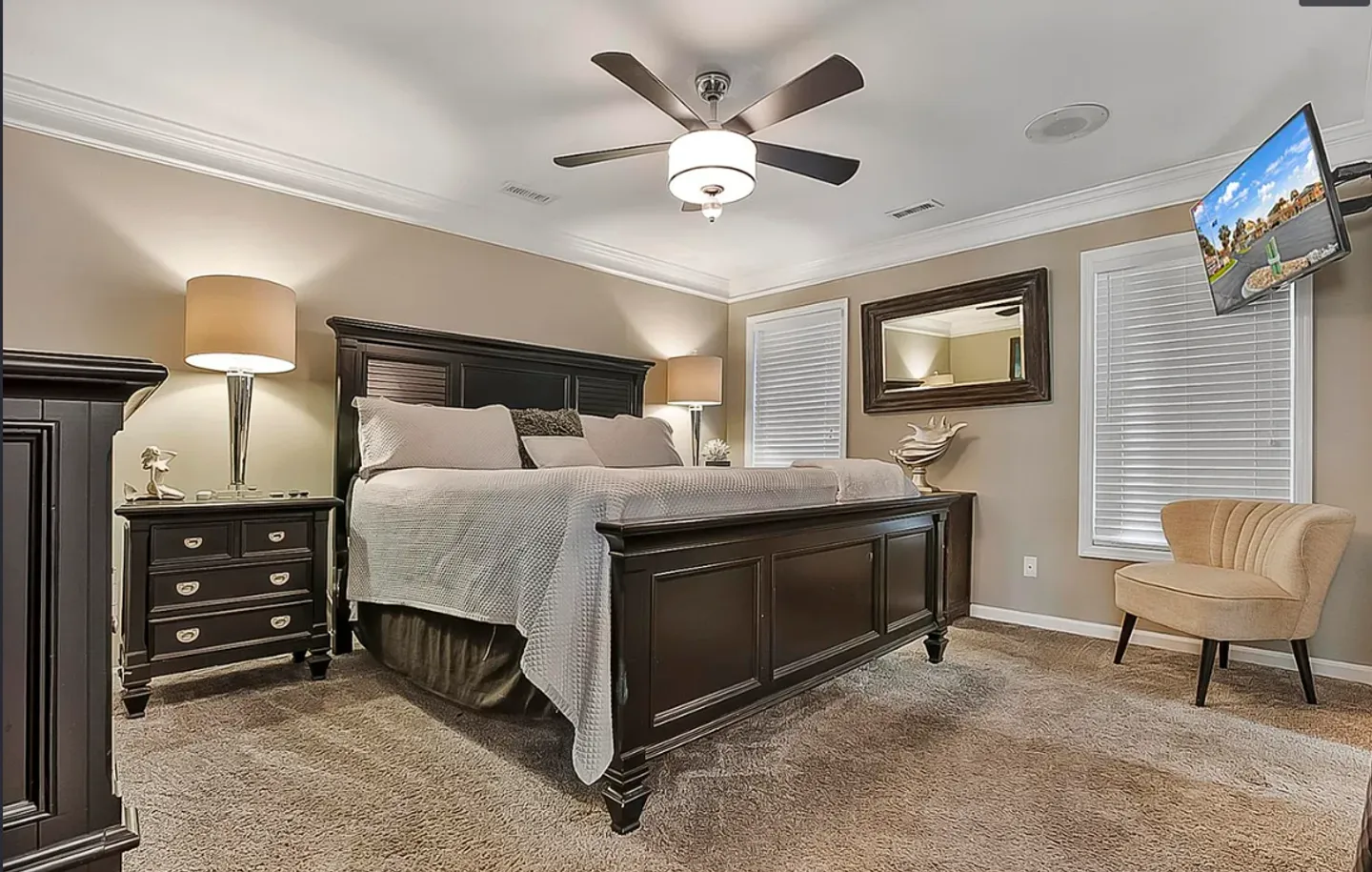 Bedroom featuring a dark wood bed frame, matching nightstand, carpeted floor, ceiling fan, and a wall-mounted TV.
