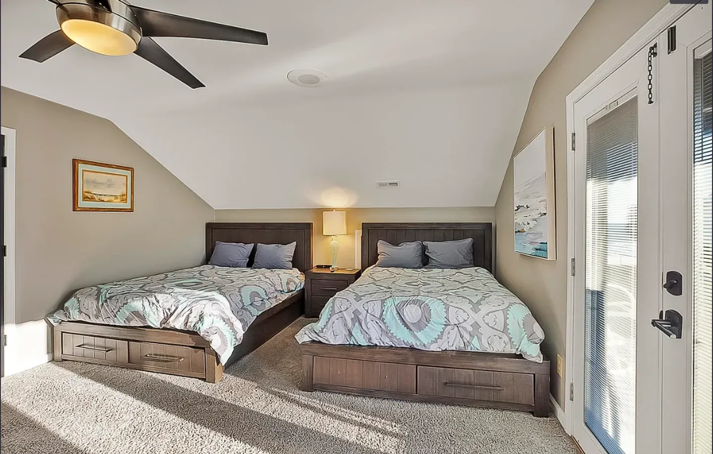 Bedroom with two wooden beds featuring built-in storage drawers, a nightstand with a lamp between them, and glass doors with blinds.