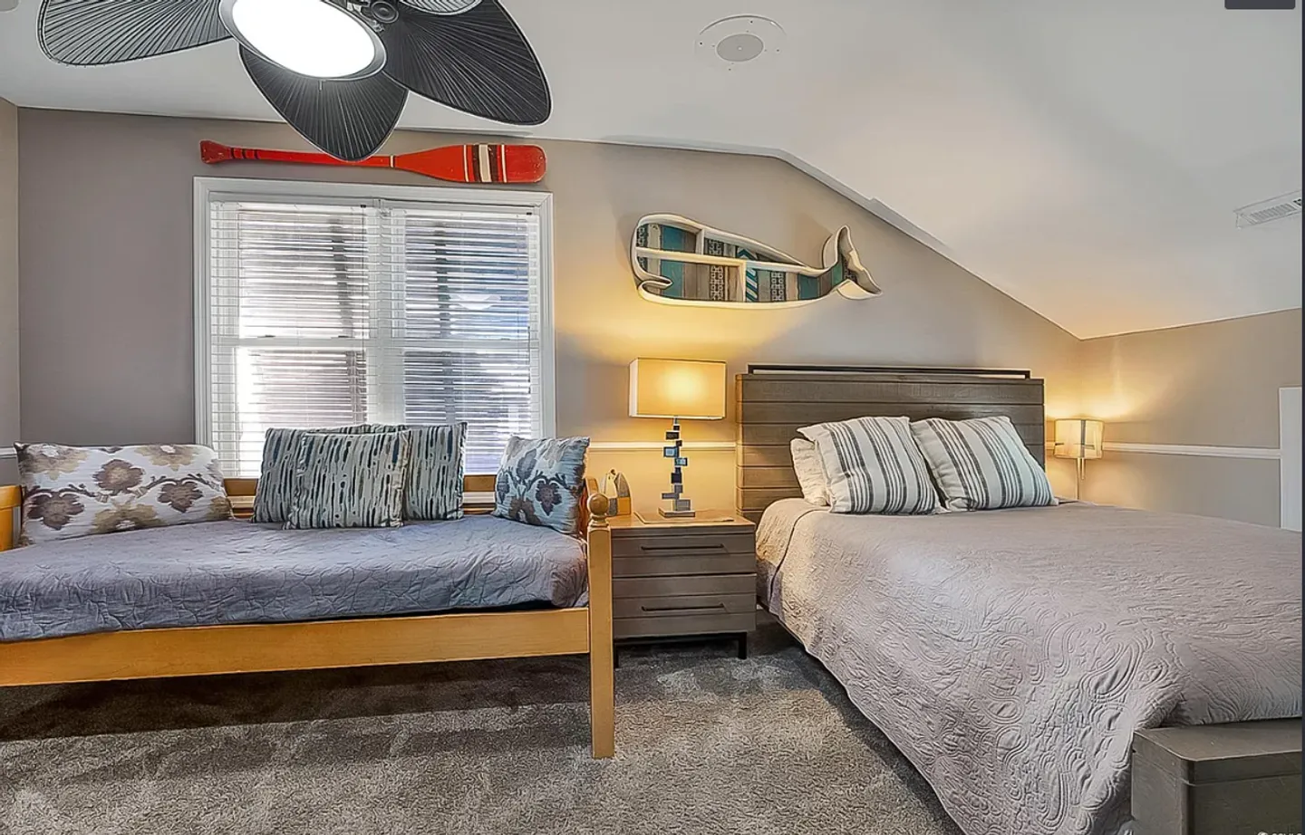 Bedroom with a bed, daybed, carpeted floor, ceiling fan, and nautical wall decor beneath a sloped ceiling.