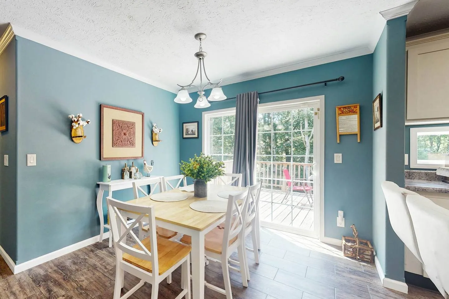 Dining area with blue walls, a light wood dining table with white chairs, and sliding glass doors leading to an outdoor deck.