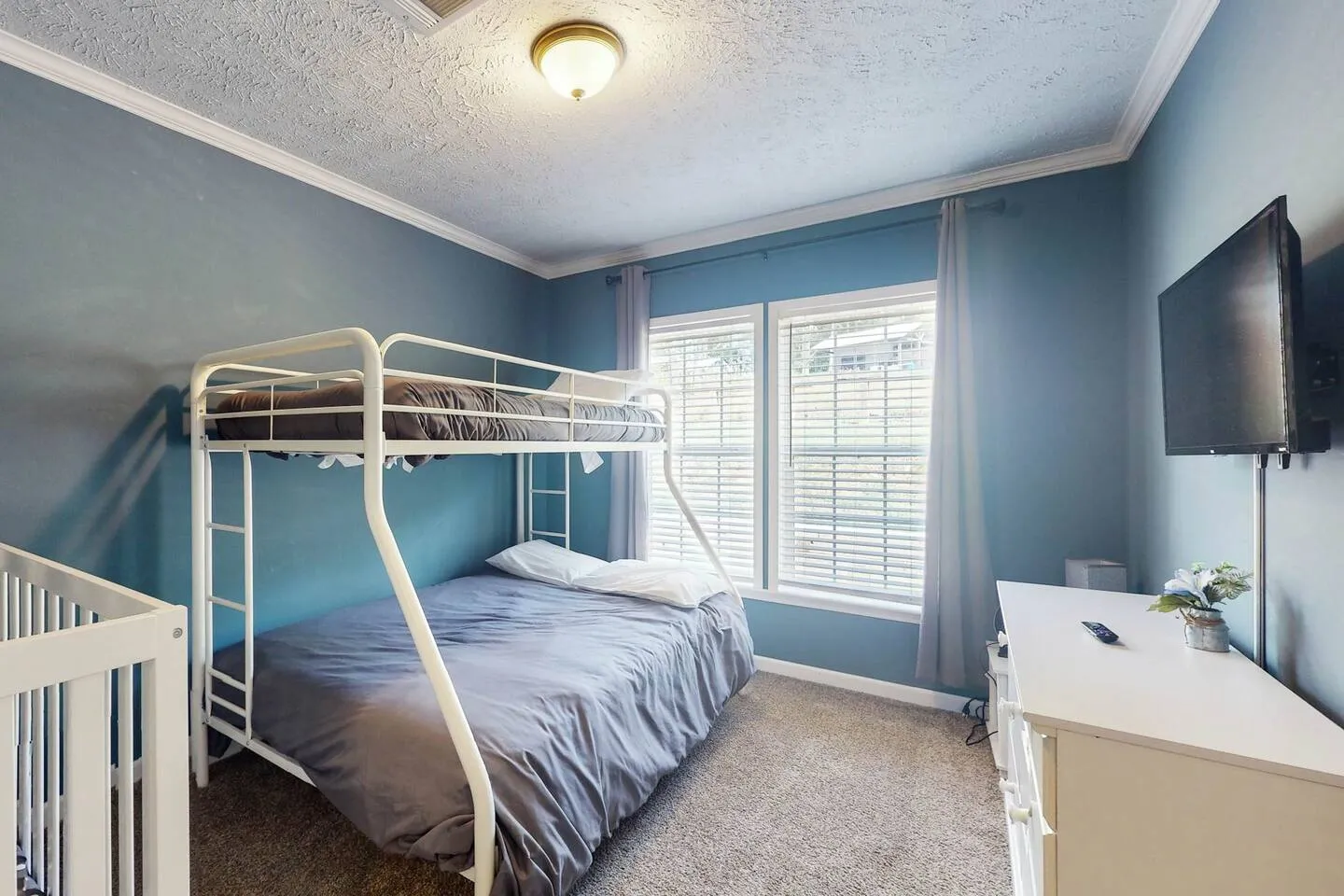 Bedroom with blue walls, carpeted floor, white metal bunk bed, and a wall-mounted TV.