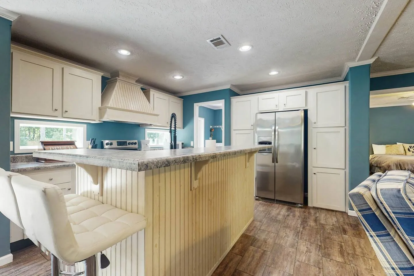 Kitchen with teal walls, white cabinetry, a beadboard island with bar seating, and stainless steel refrigerator.