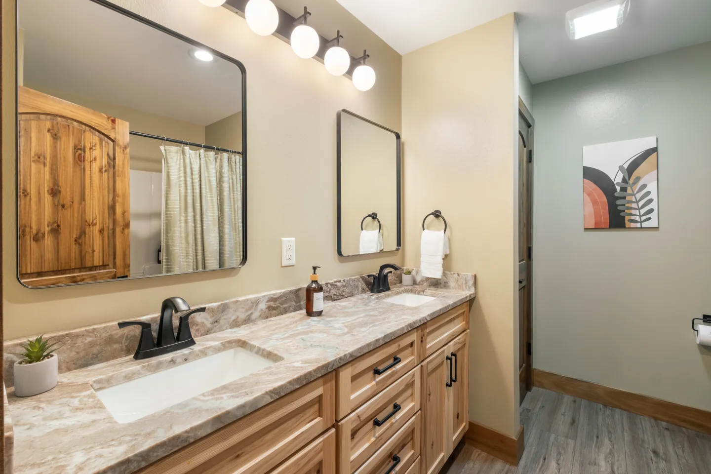 Bathroom vanity with dual undermount sinks, patterned countertop, light wood cabinetry, and two black-framed mirrors.