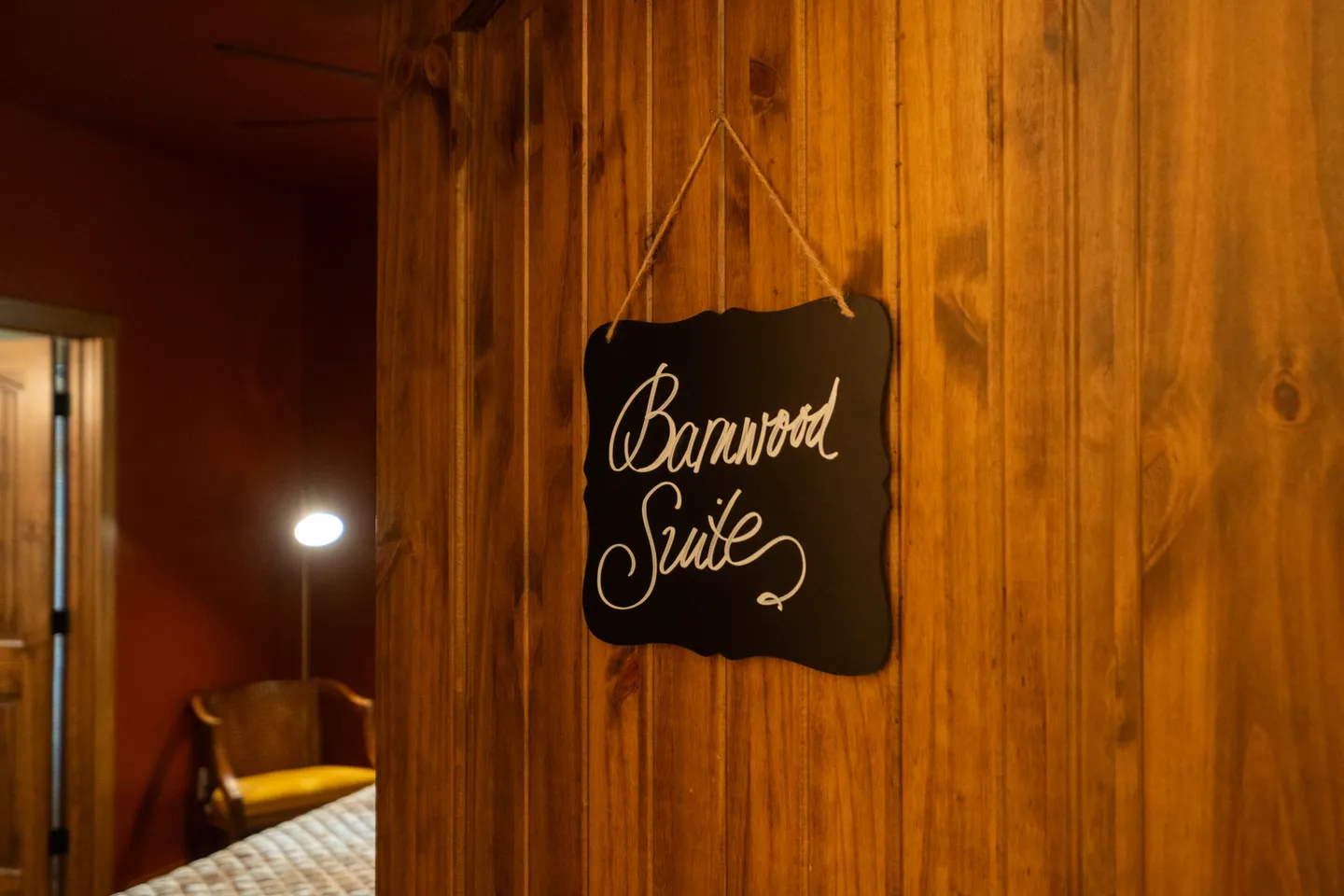A wooden door with a hanging sign that reads 'Barnwood Suite' leading into a bedroom.