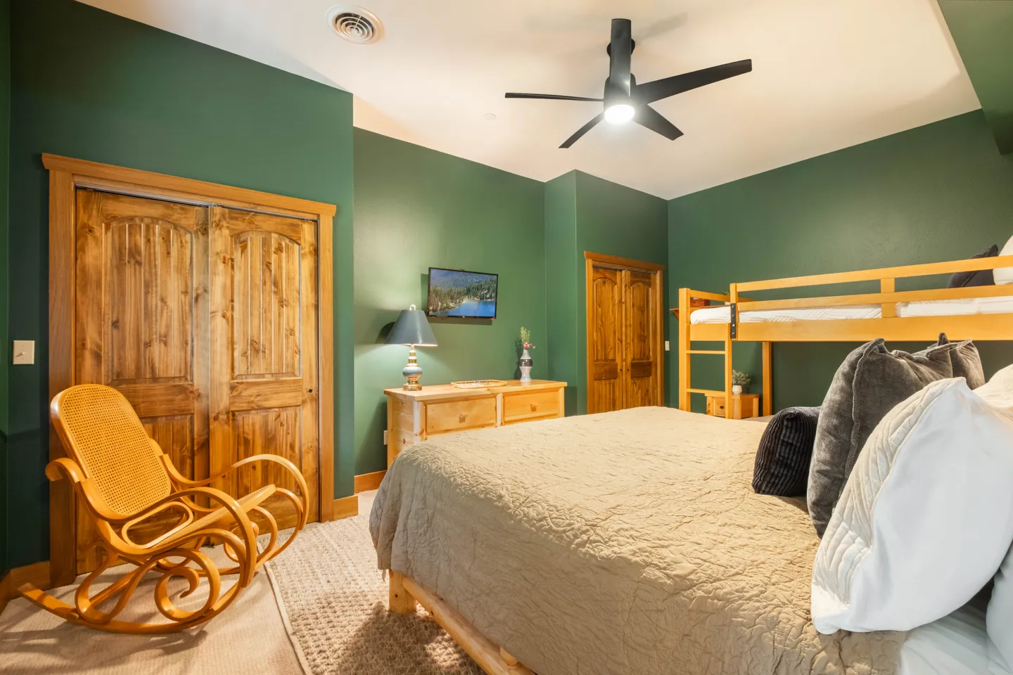 Bedroom with forest green walls, a bed in the foreground, bunk beds, a rocking chair, and natural wood doors.