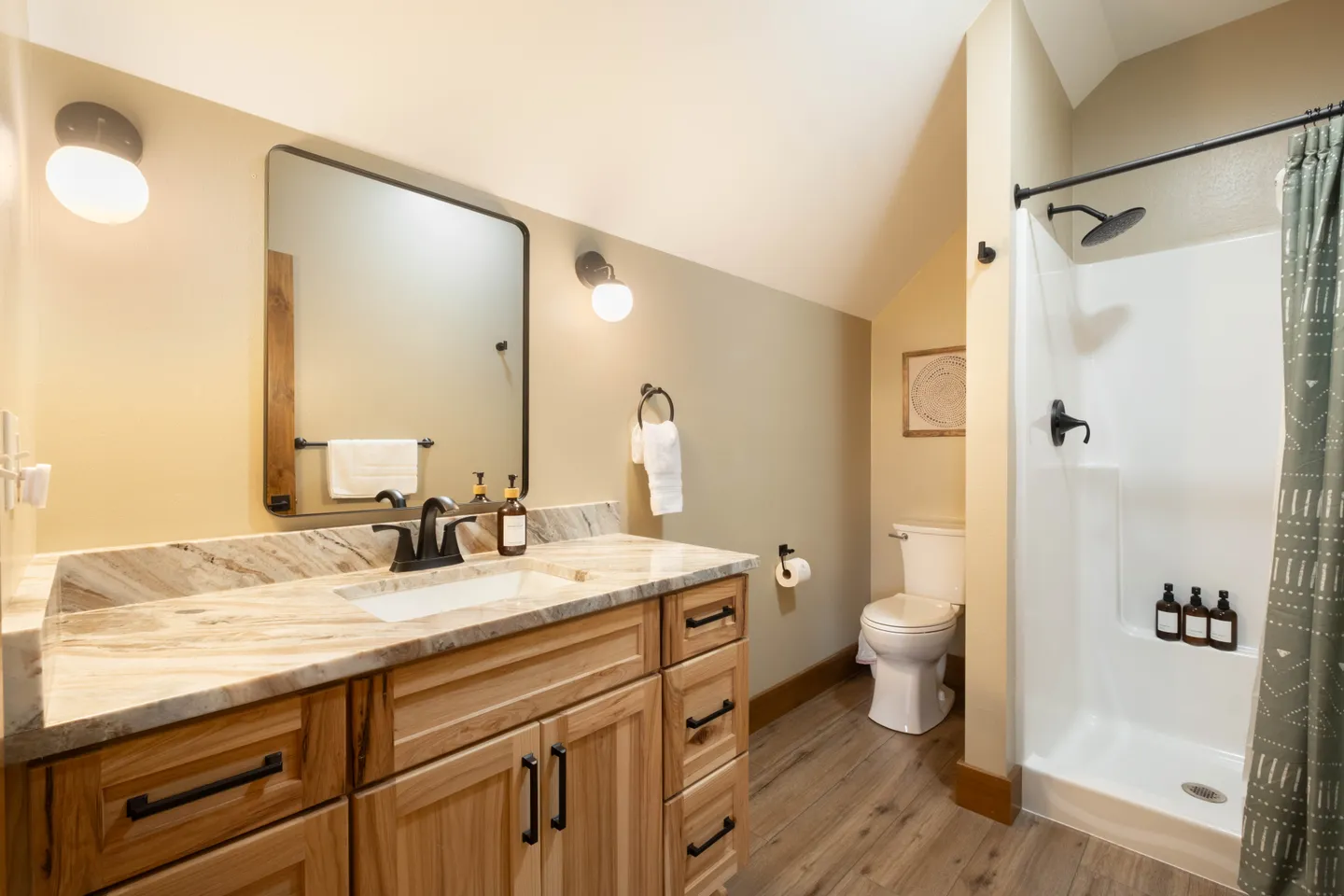 Bathroom with a wood vanity, marbled countertop, rectangular mirror, toilet, and walk-in shower with a curtain.