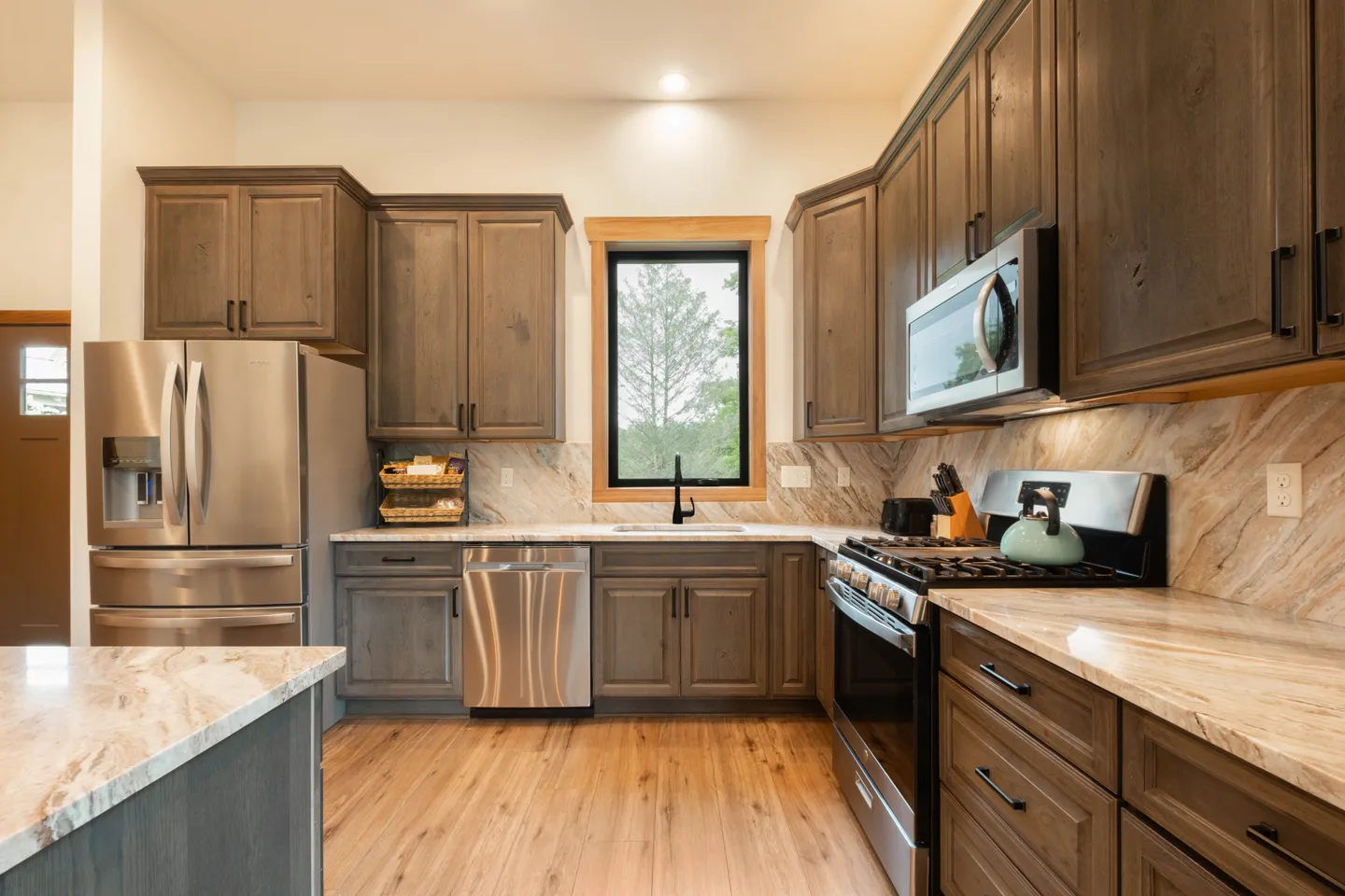 Kitchen with dark wood cabinets, light stone countertops, stainless steel appliances, and a window above the sink.