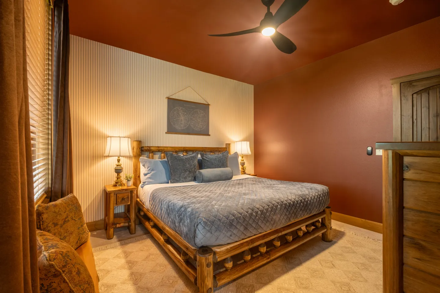 Bedroom featuring a log-style wooden bed, bedside tables with lamps, a modern ceiling fan, and rust-colored walls.