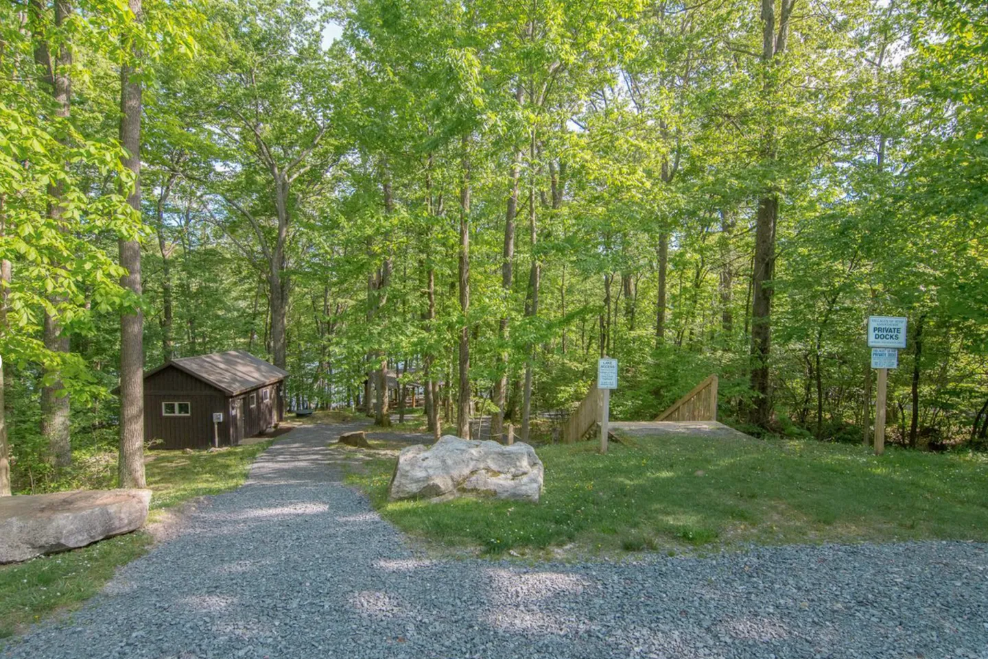 A gravel pathway leading through a wooded area toward a small cabin and a path to private docks.