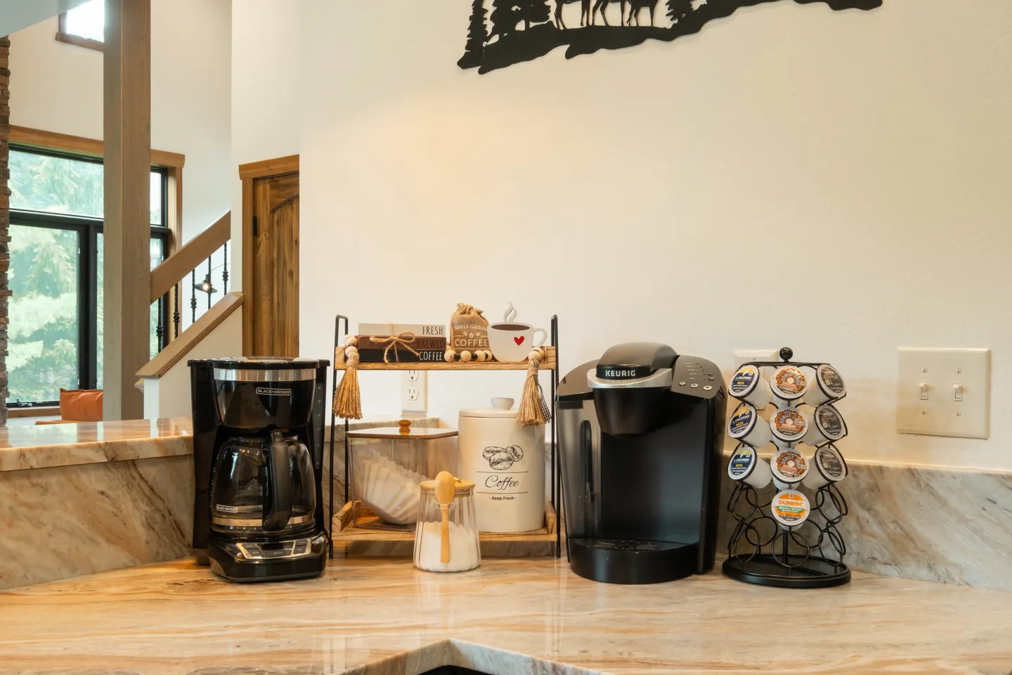 Close-up of a coffee bar station on a patterned countertop with drip and single-serve coffee makers, canisters, and a pod carousel.