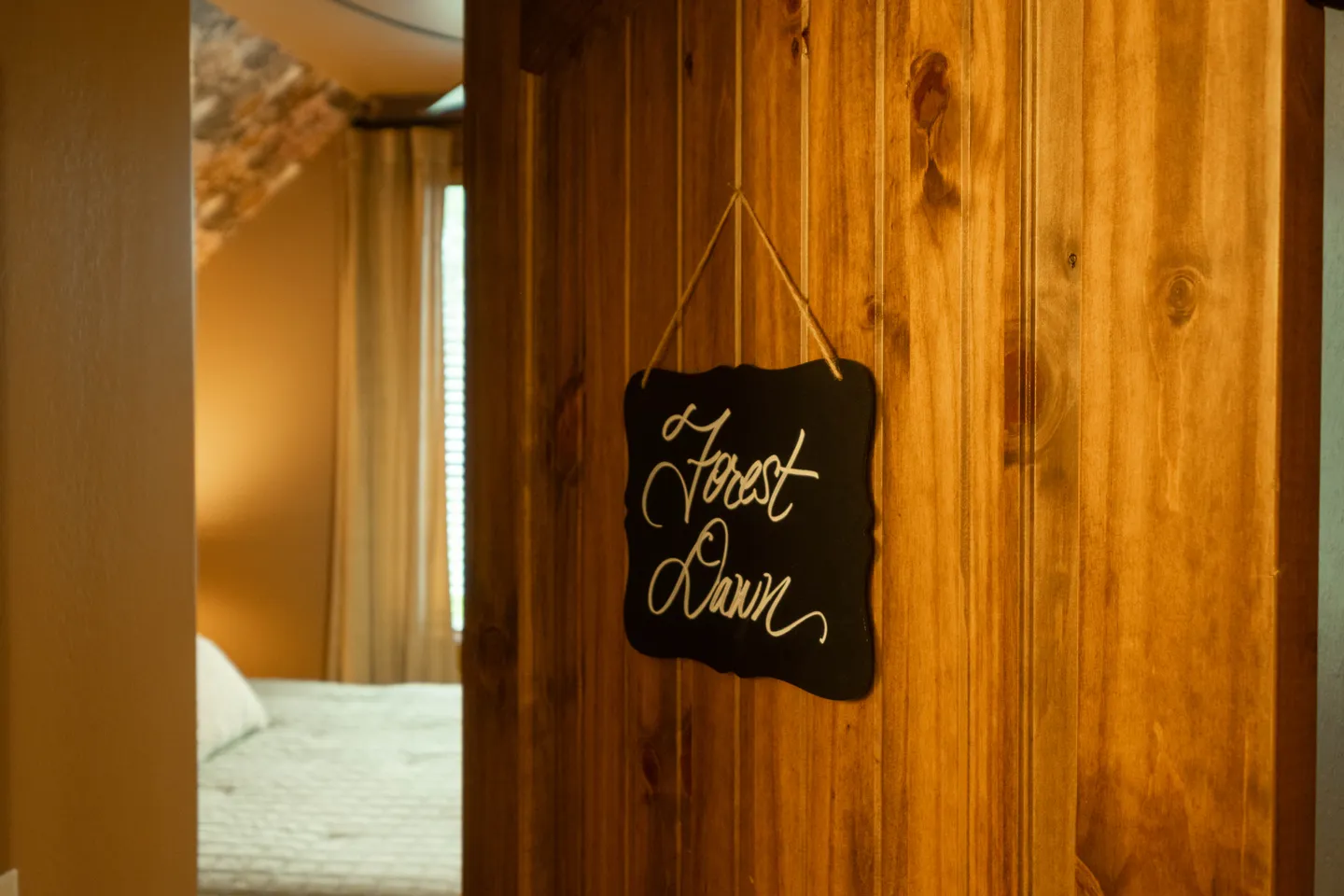 Close-up of a wooden bedroom door with a hanging sign that reads 'Forest Dawn', looking into the bedroom.