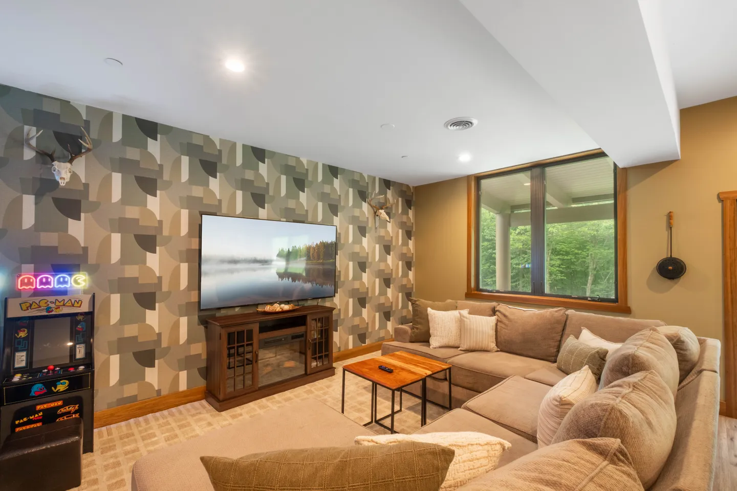 Living room with a large sectional sofa, wall-mounted television over a fireplace media console, geometric patterned accent wall, and a Pac-Man arcade cabinet.