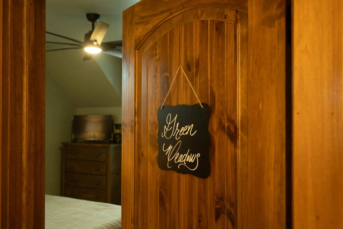 A wooden door with a hanging sign that reads 'Green Meadows' opening into a bedroom.