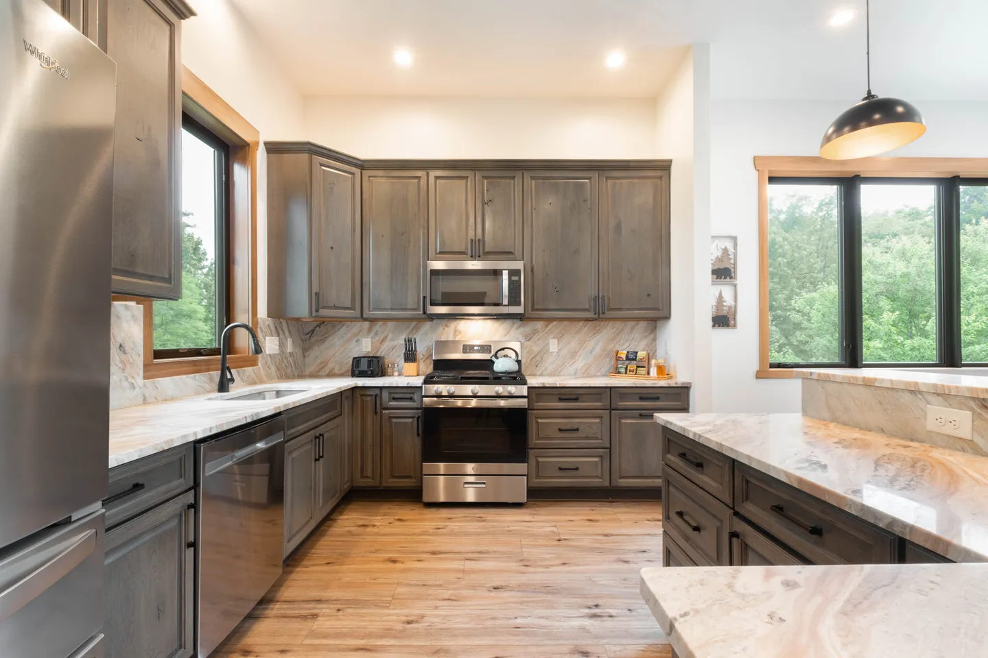Kitchen featuring weathered gray wooden cabinetry, patterned stone countertops, stainless steel appliances, and wood-look flooring.