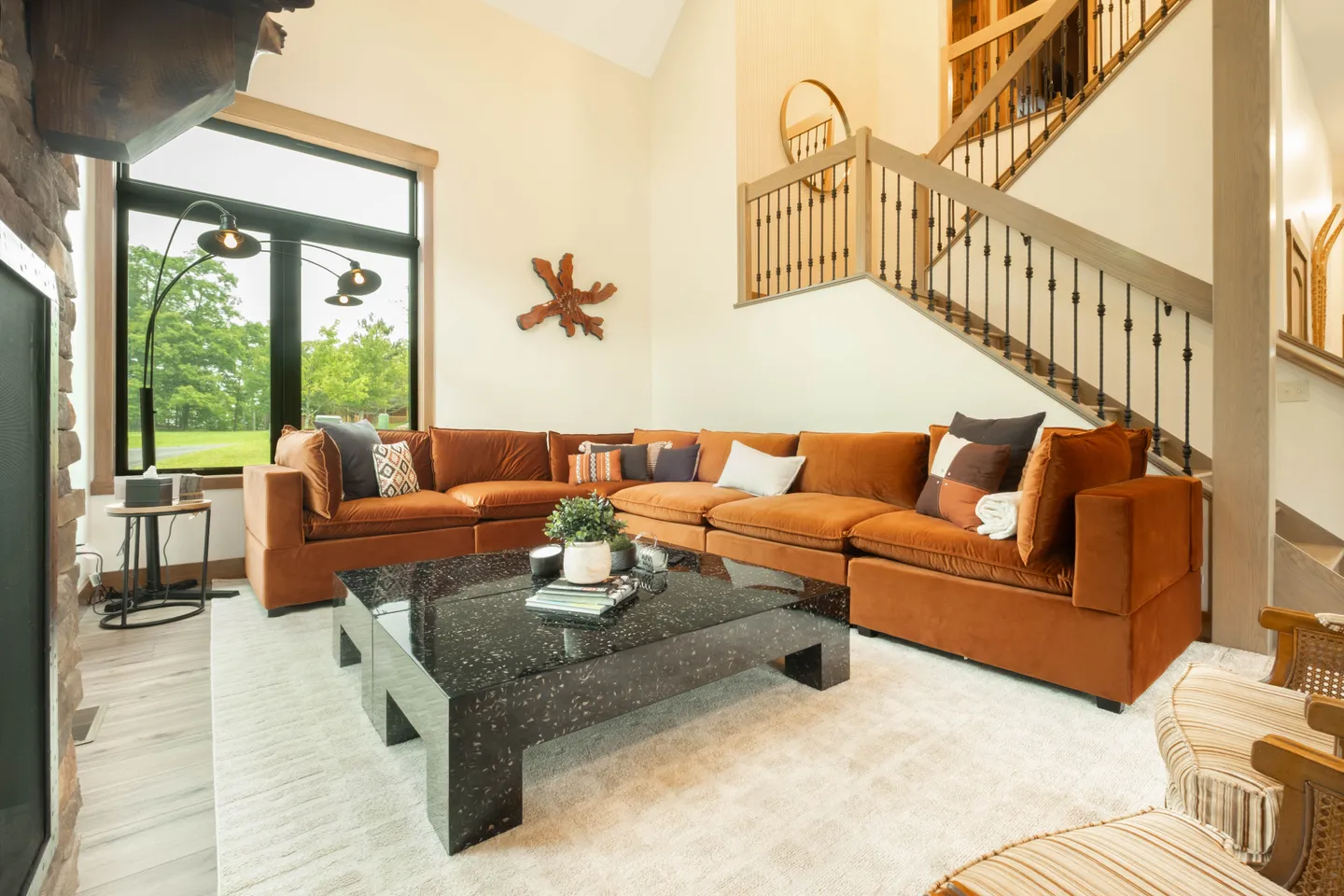 Living room with an L-shaped burnt orange sectional sofa, dark terrazzo coffee table, and an open staircase.