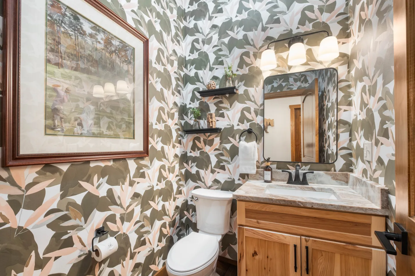 Powder room with patterned botanical wallpaper, a light wood vanity, toilet, and framed artwork.