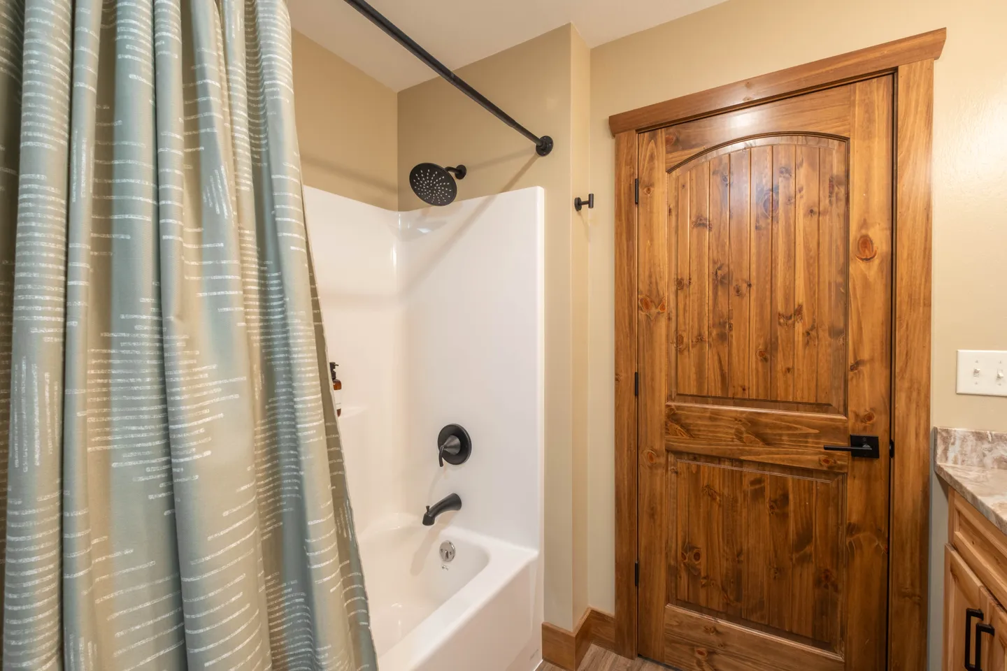 Bathroom with a bathtub shower combination featuring matte black fixtures next to a rustic wooden door.