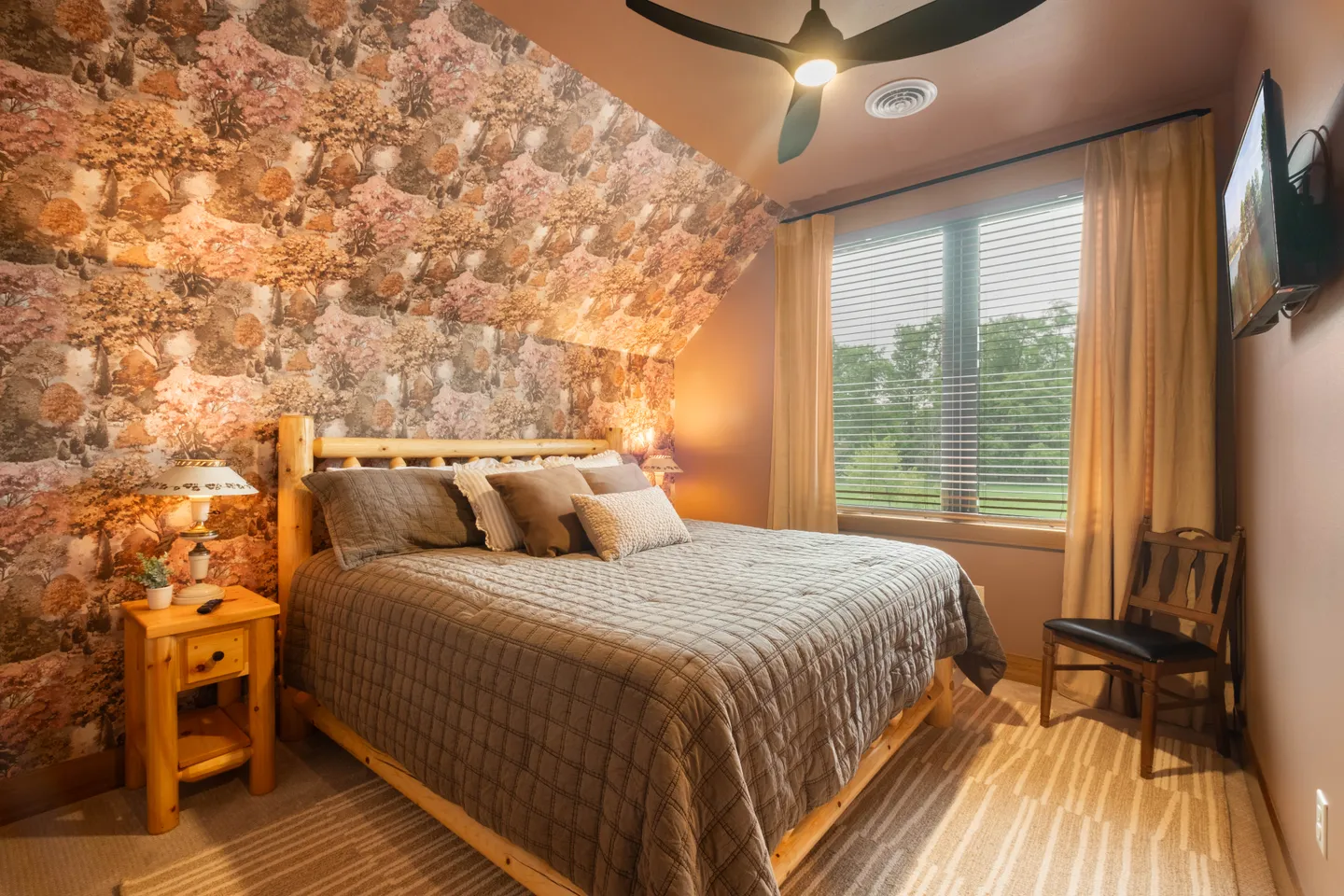 Bedroom featuring a log-style bed frame against a floral-patterned accent wall with a sloped ceiling and a large window.