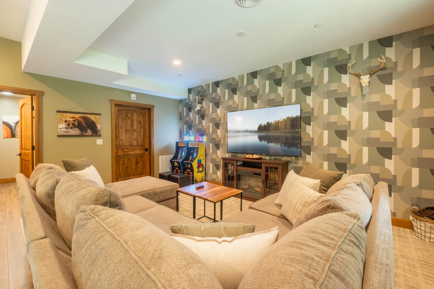 Living room featuring a large sectional sofa, coffee table, wall-mounted television, and arcade game machines against a patterned accent wall.