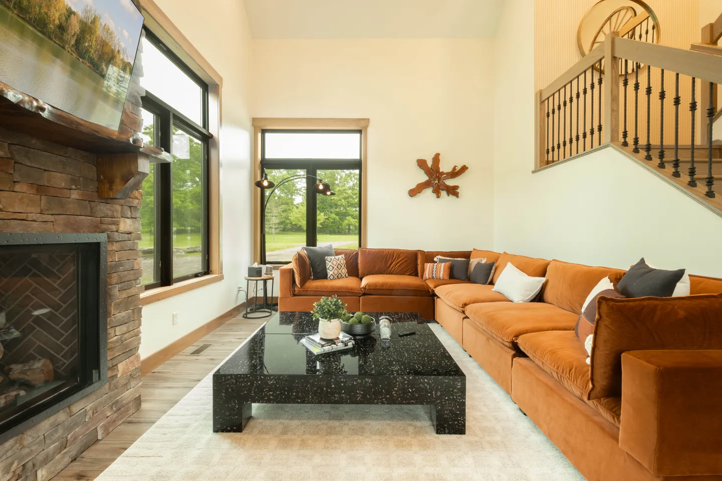 Living room with a large rust-orange sectional sofa, black speckled coffee table, and a stone fireplace with a television mounted above.