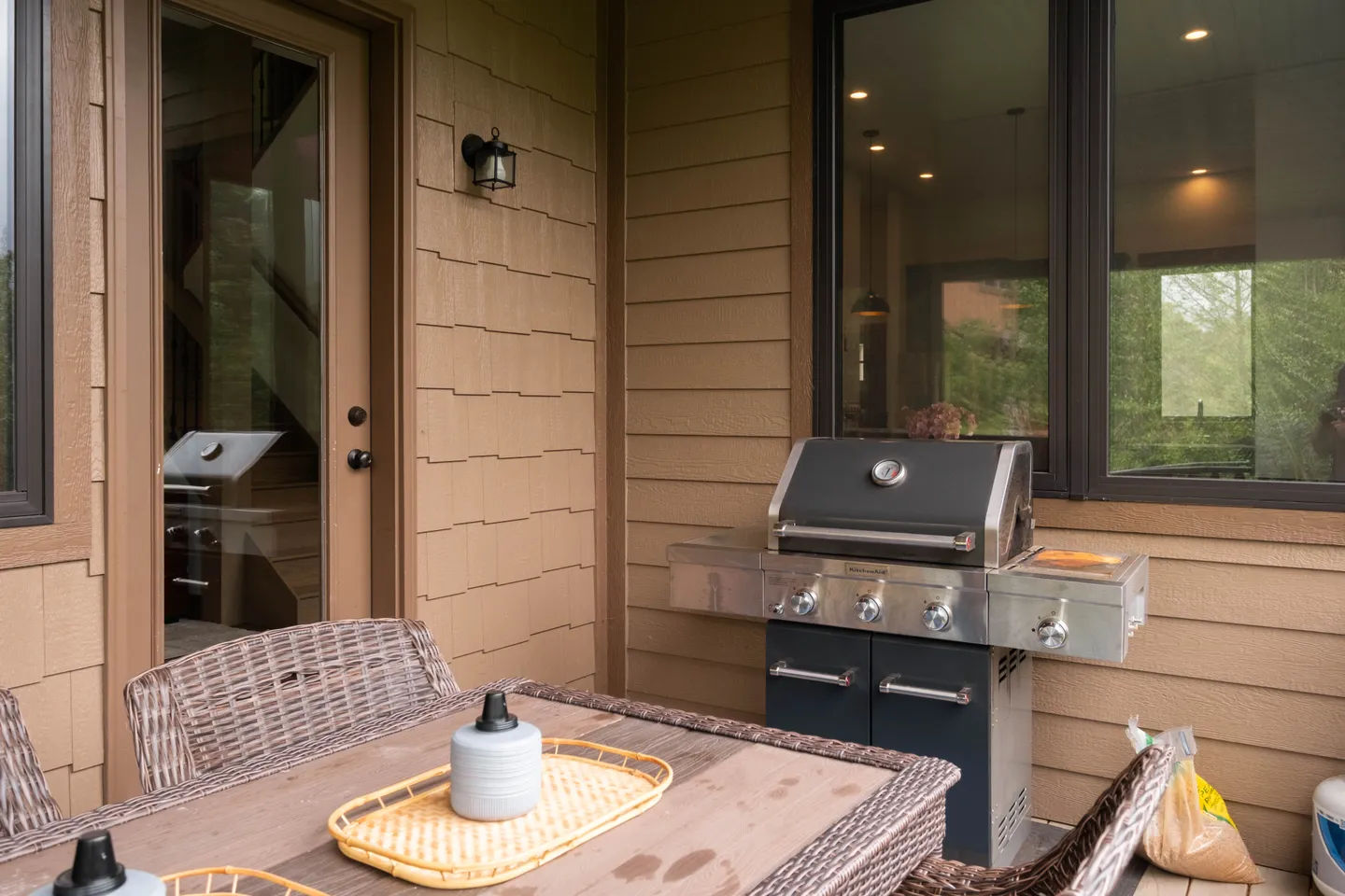 Outdoor deck with a freestanding stainless steel and black gas grill beside an outdoor dining table with wicker chairs.