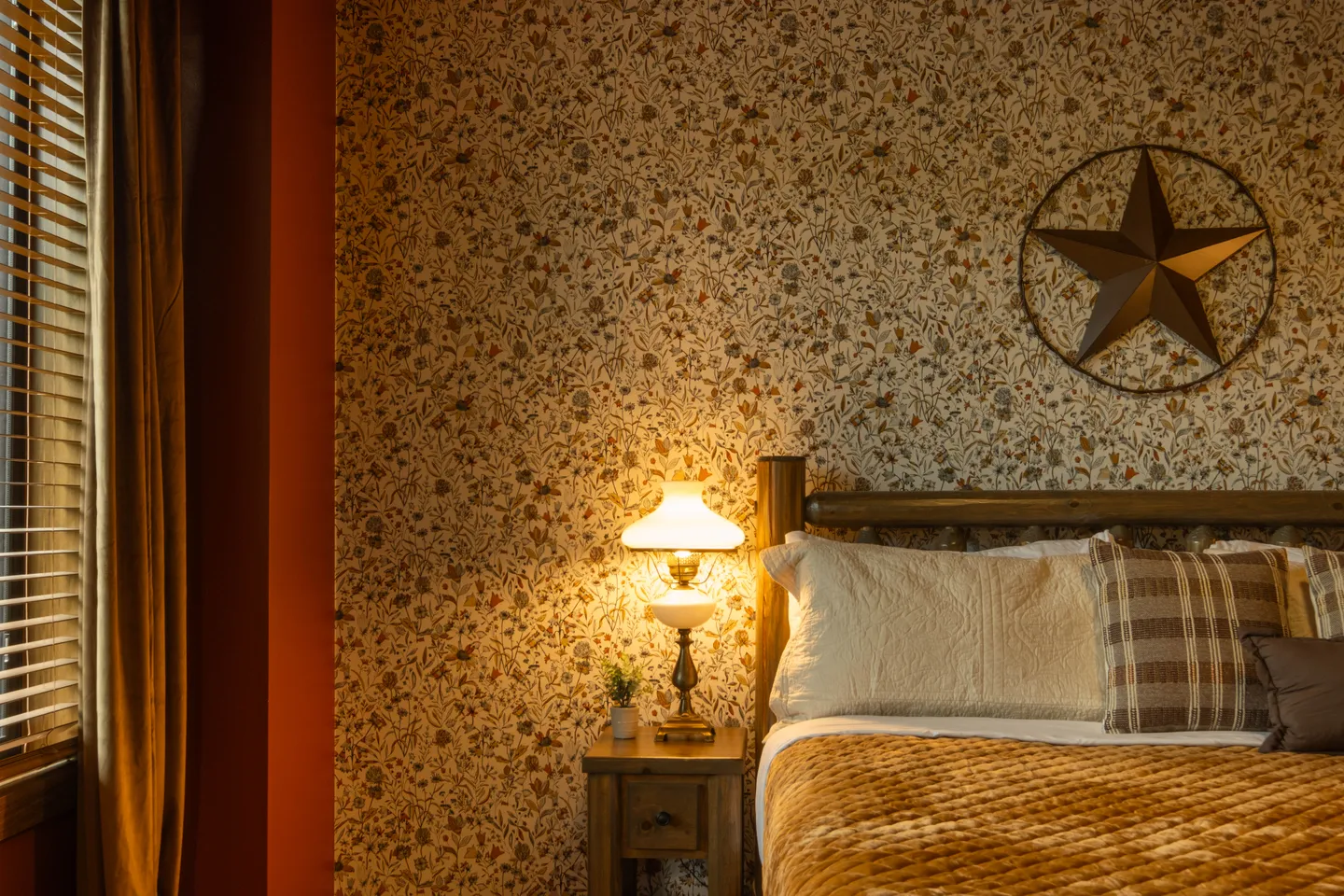 Bedroom detail featuring floral wallpaper, a wood nightstand with a lit lamp, and a made bed.