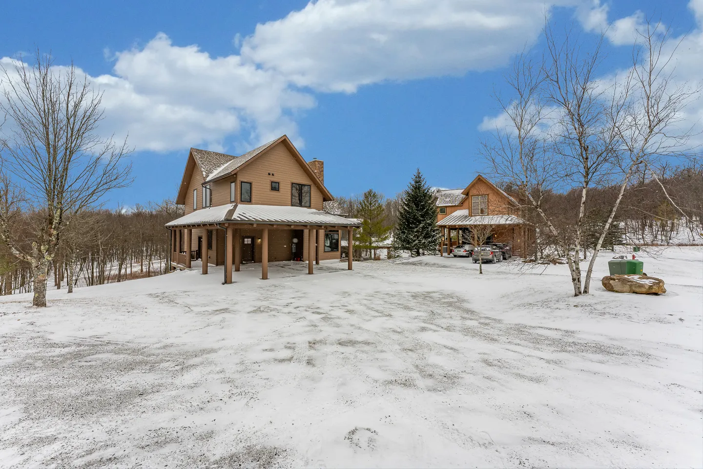 Exterior view of two multi-story brown homes on a snow-covered property under a partly cloudy sky.