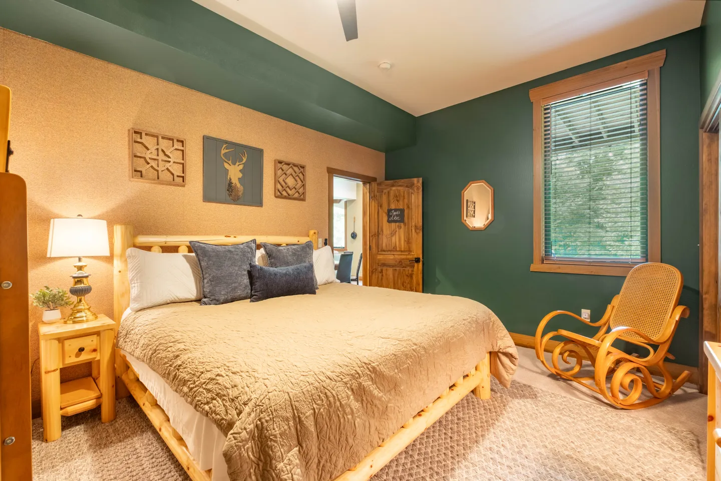 Bedroom featuring a log-style bed frame with a tan bedspread, green accent walls, a matching wooden nightstand, and a rocking chair.