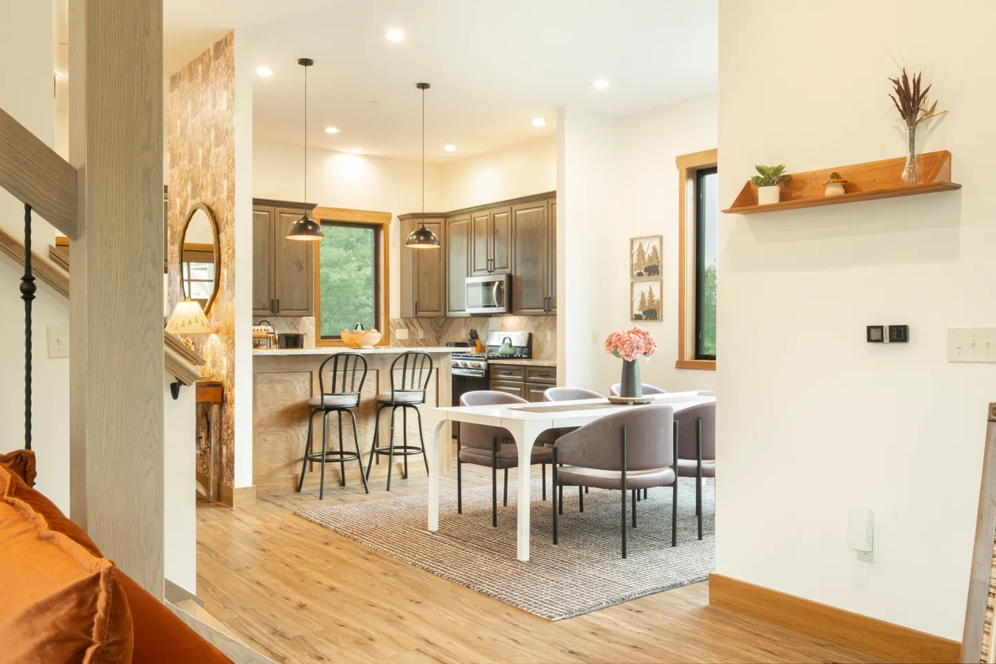 Open concept dining area and kitchen with wood-look flooring, dining table with modern armchairs, and a kitchen island with barstools.