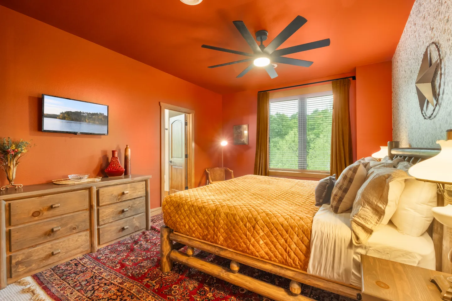 Bedroom with bold orange walls and ceiling, a log-style bed, a patterned area rug, a ceiling fan, and a window with blinds.