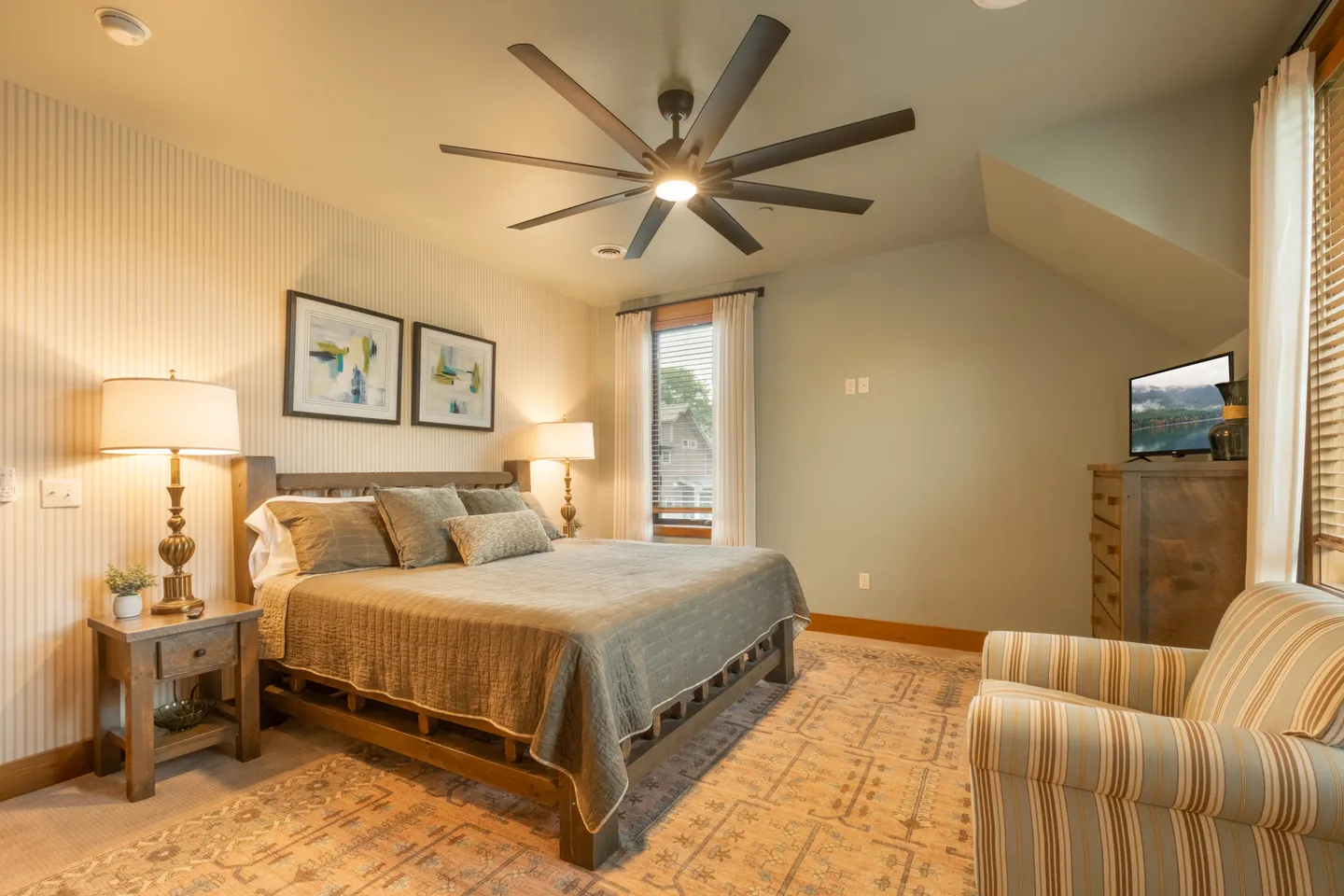 Bedroom featuring a wooden bed, patterned area rug, large ceiling fan, and an armchair in the foreground.