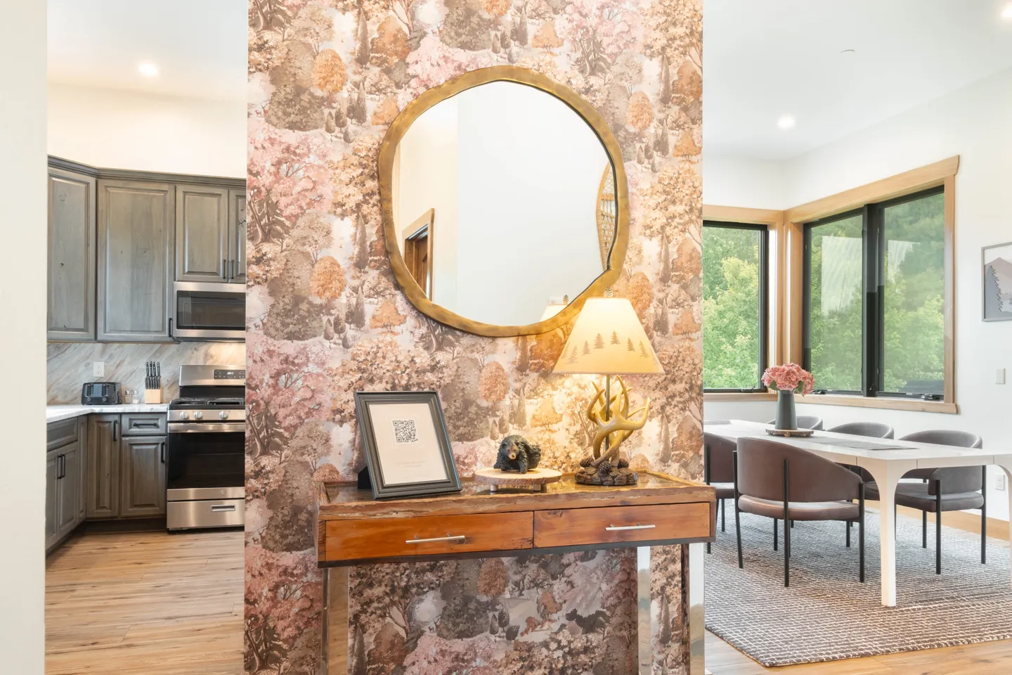 Entry console table with an antler lamp and mirror in front of wallpaper, flanked by views into a kitchen and dining area.