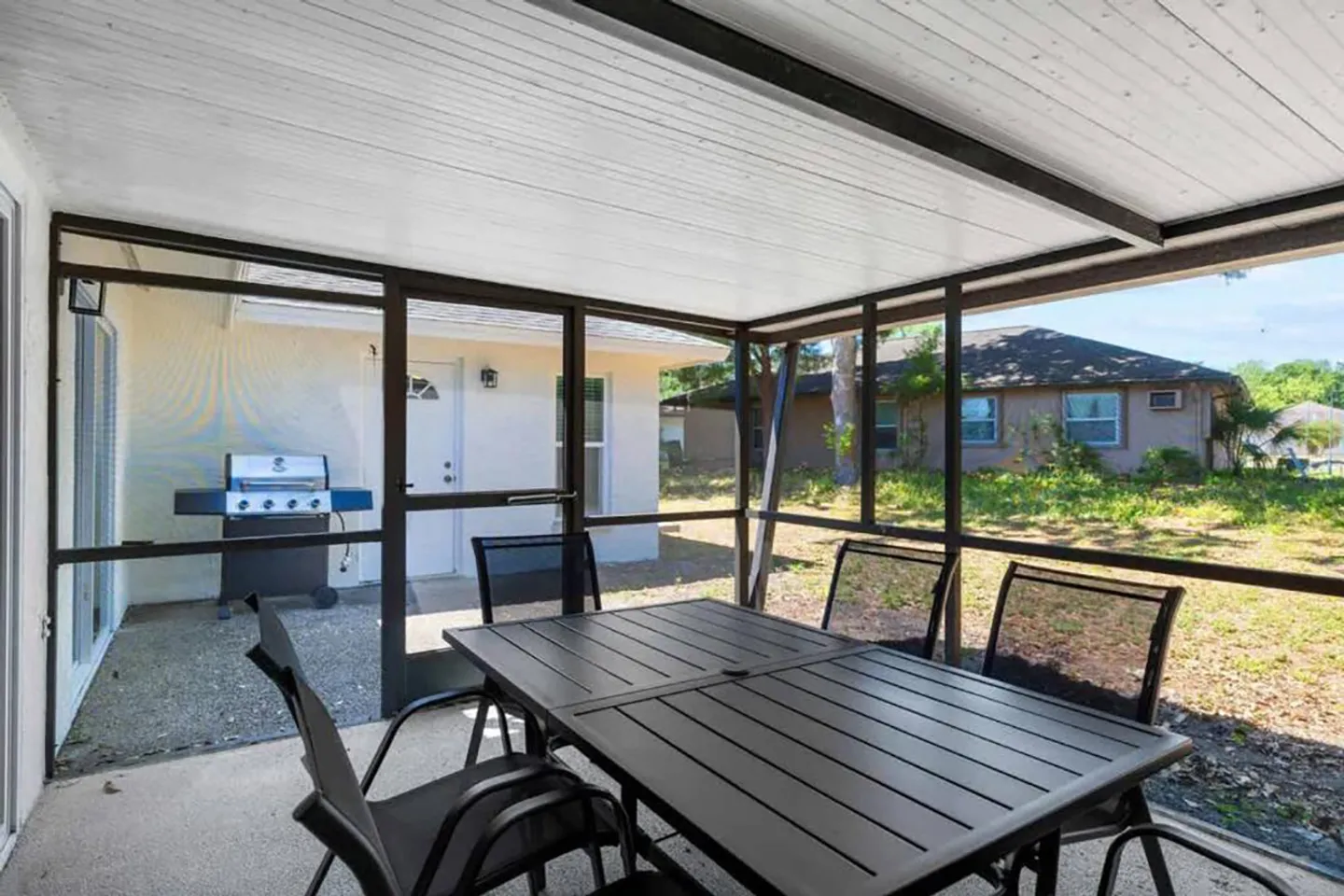 Screened-in patio with an outdoor dining table and chairs overlooking the yard and an exterior patio with a barbecue grill.