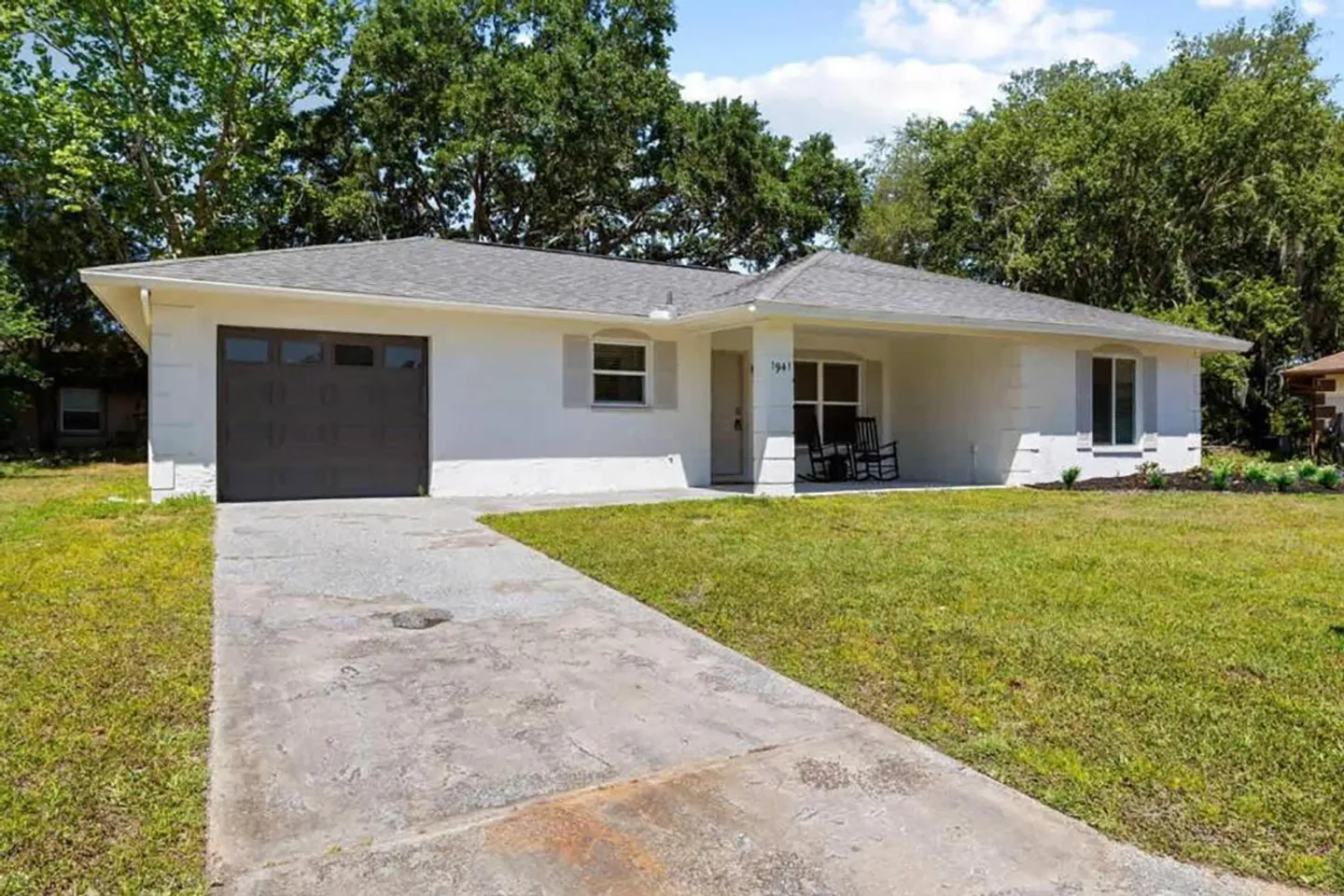 Front exterior of a single-story white home with a garage, covered porch, and concrete driveway.