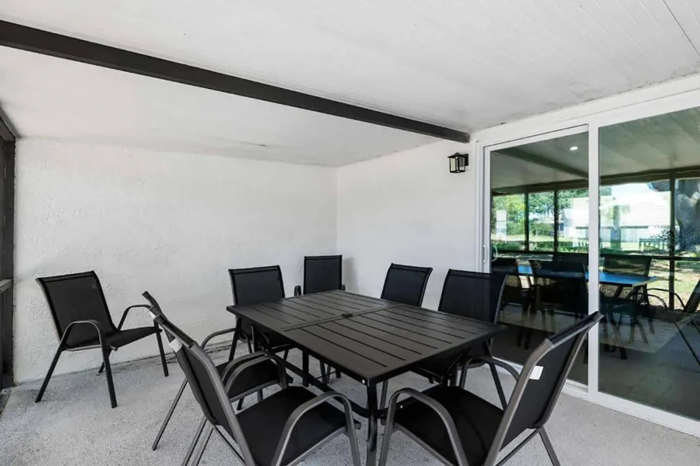 A covered patio with a black slatted dining table and matching chairs next to sliding glass doors.