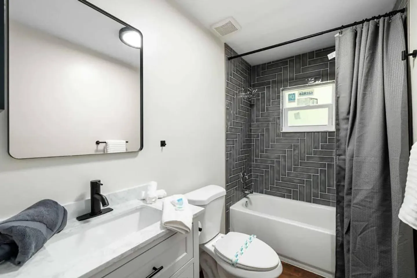 Bathroom with white vanity, toilet, and bathtub with dark herringbone tile surround