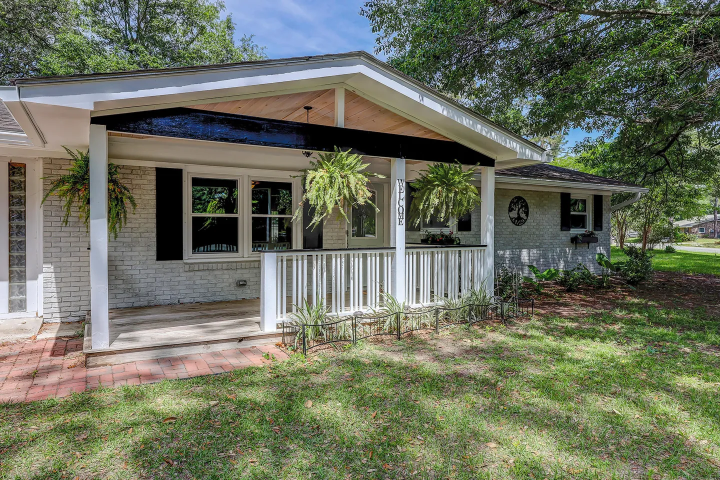 Exterior front covered porch of a painted brick home with hanging plants, white railings, and a brick walkway.