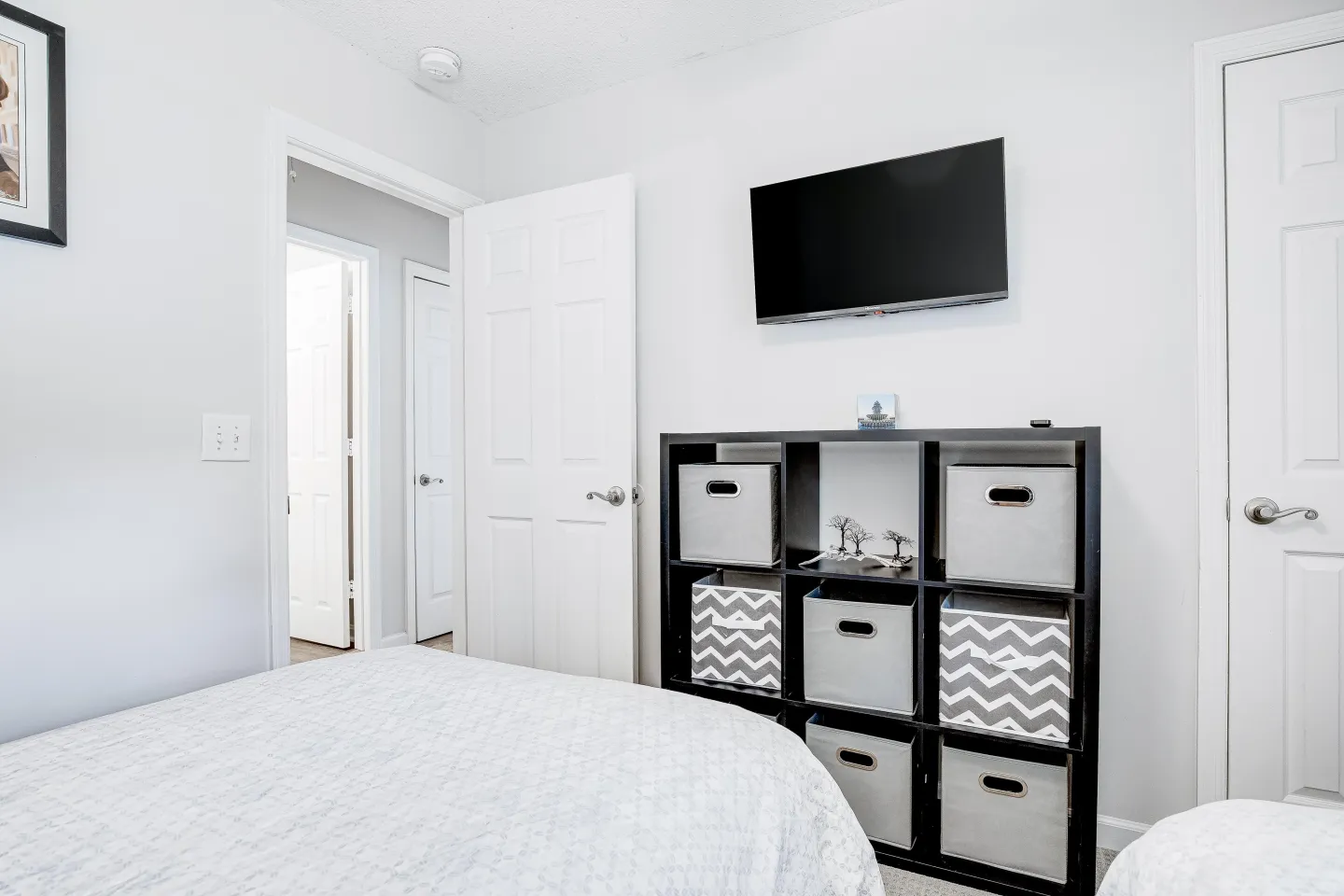 Bedroom featuring a bed with a light-colored quilt, a black cubby shelving unit with fabric storage bins, and a wall-mounted flat-screen TV.
