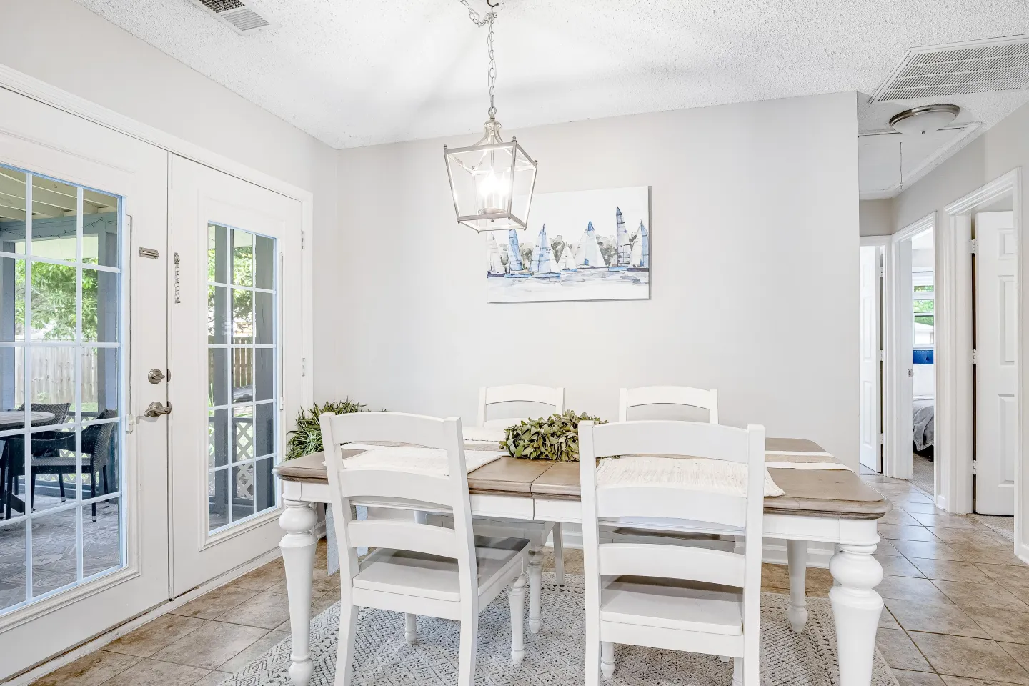 Dining area with a wooden table, white chairs, a pendant light, and glass patio doors leading outside.