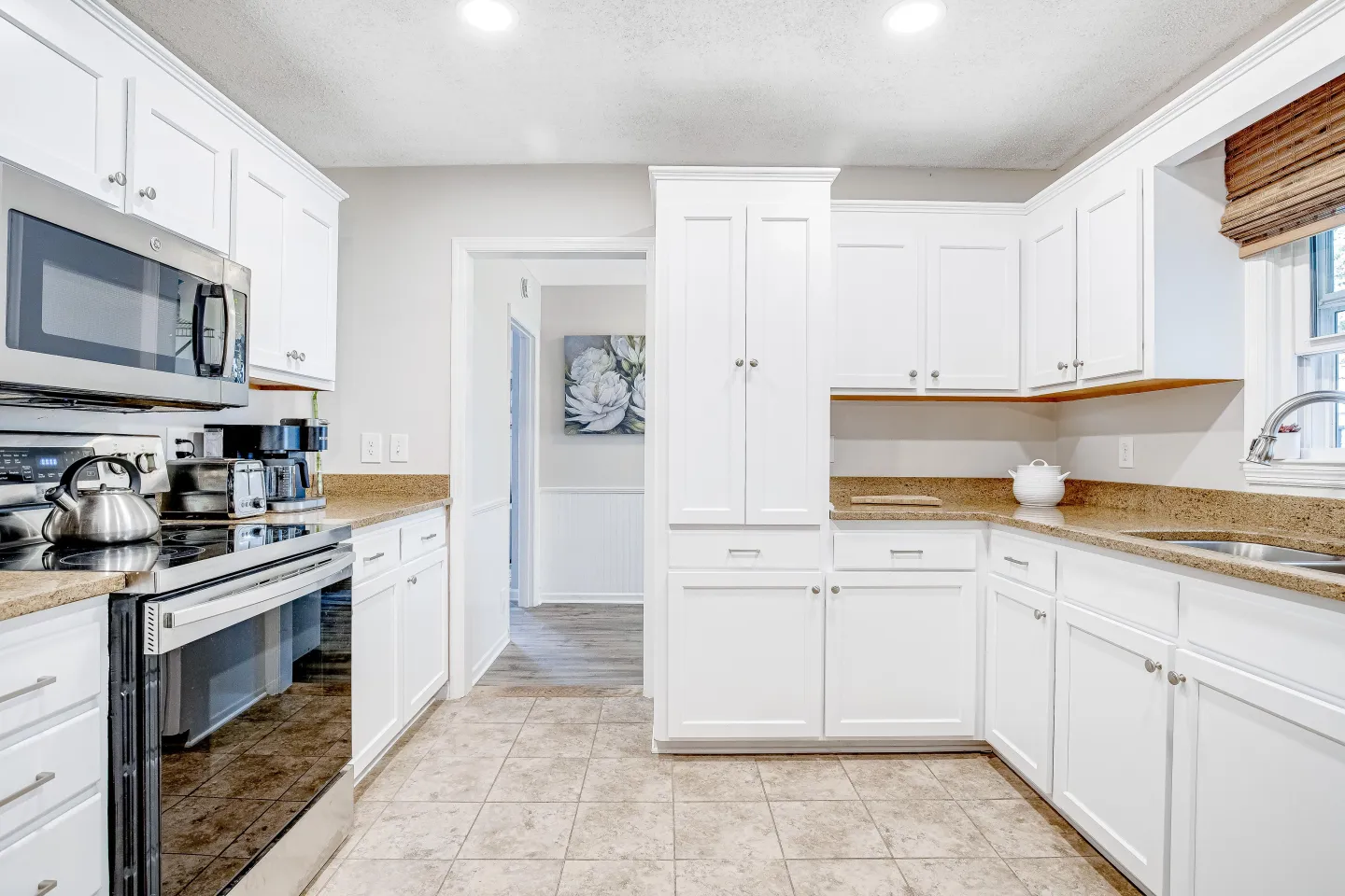 Bright kitchen featuring white cabinets, speckled brown countertops, stainless steel appliances, and tiled flooring.