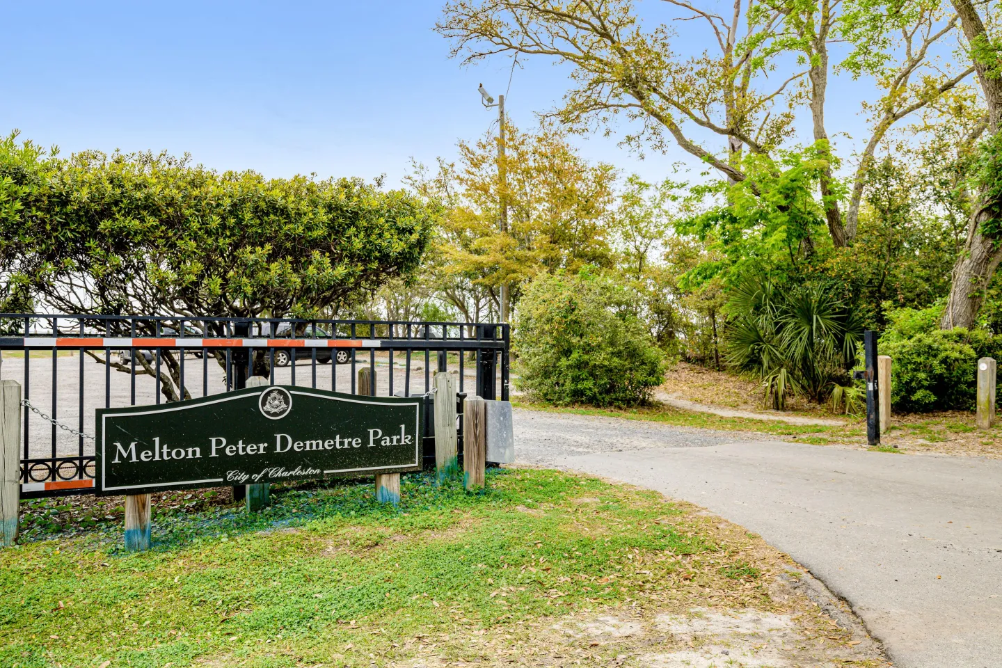 Entrance sign for Melton Peter Demetre Park beside a paved driveway, gate, and trees.