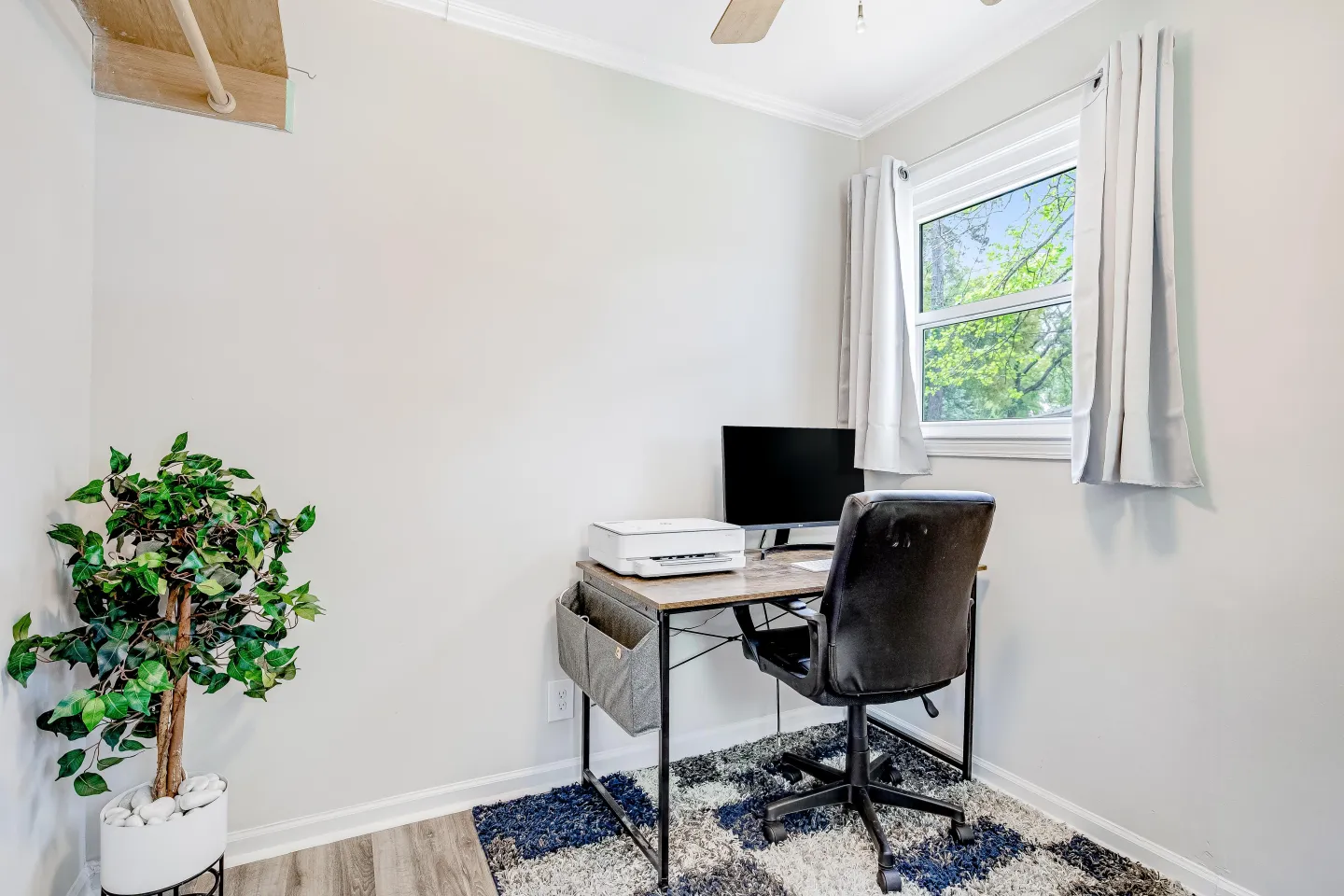Dedicated workspace with a small wooden desk, rolling office chair, monitor, printer, and window.