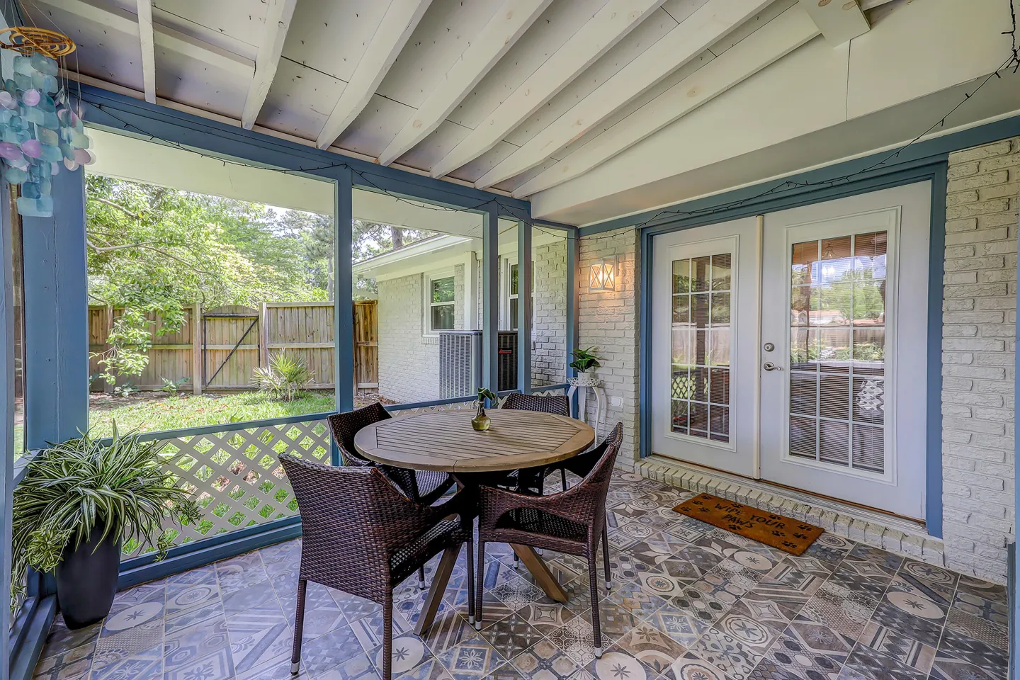 Screened-in porch with patterned tile flooring, a circular wooden table with woven chairs, and views of a fenced backyard.