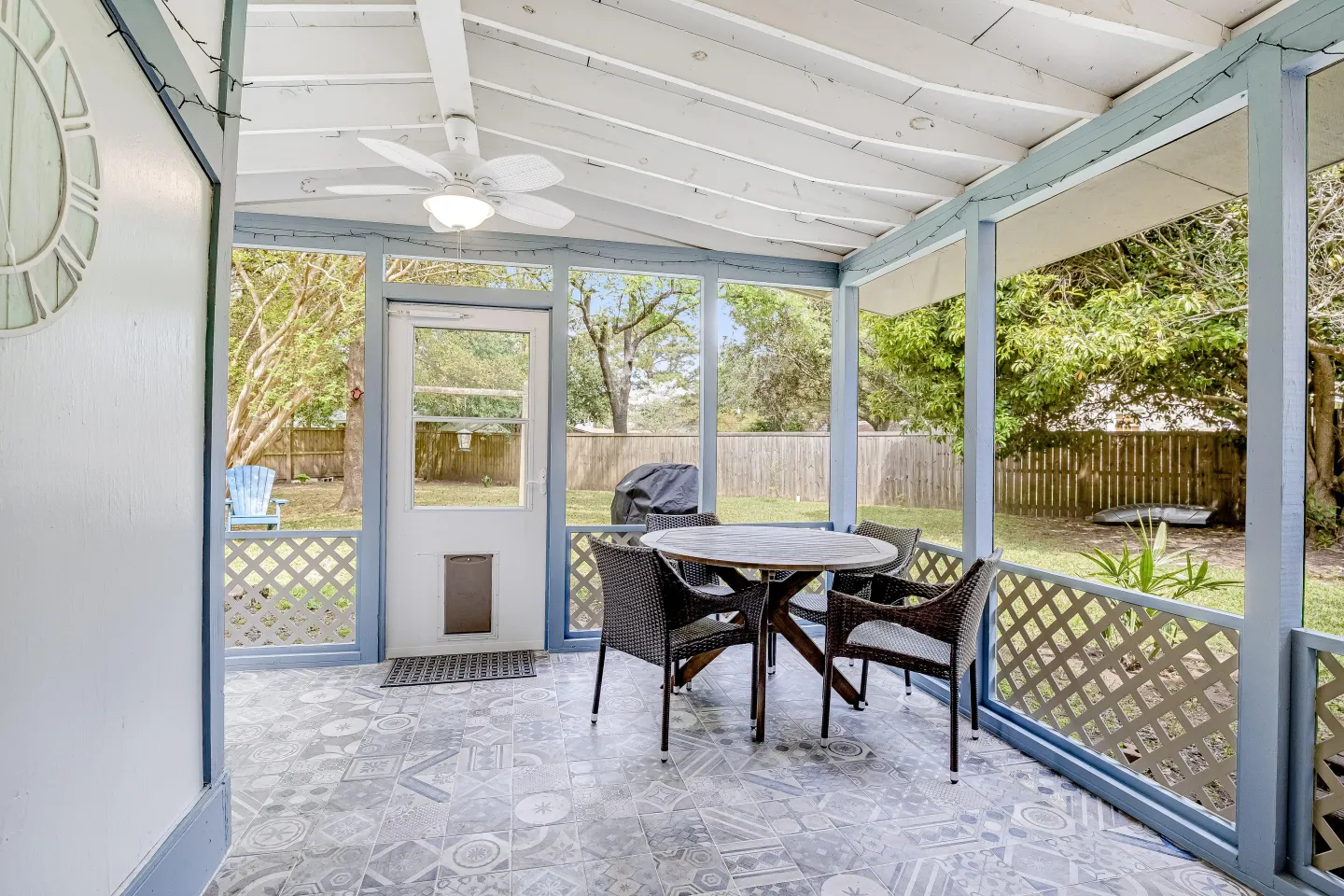 Screened porch with patterned tile flooring, a dining table with wicker chairs, a ceiling fan, and views of a fenced backyard.