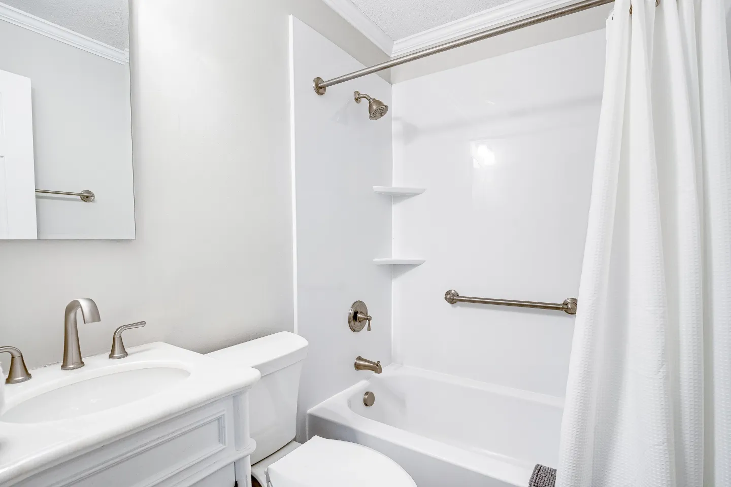 Bathroom with a white vanity, toilet, and bathtub-shower combination with white surround.
